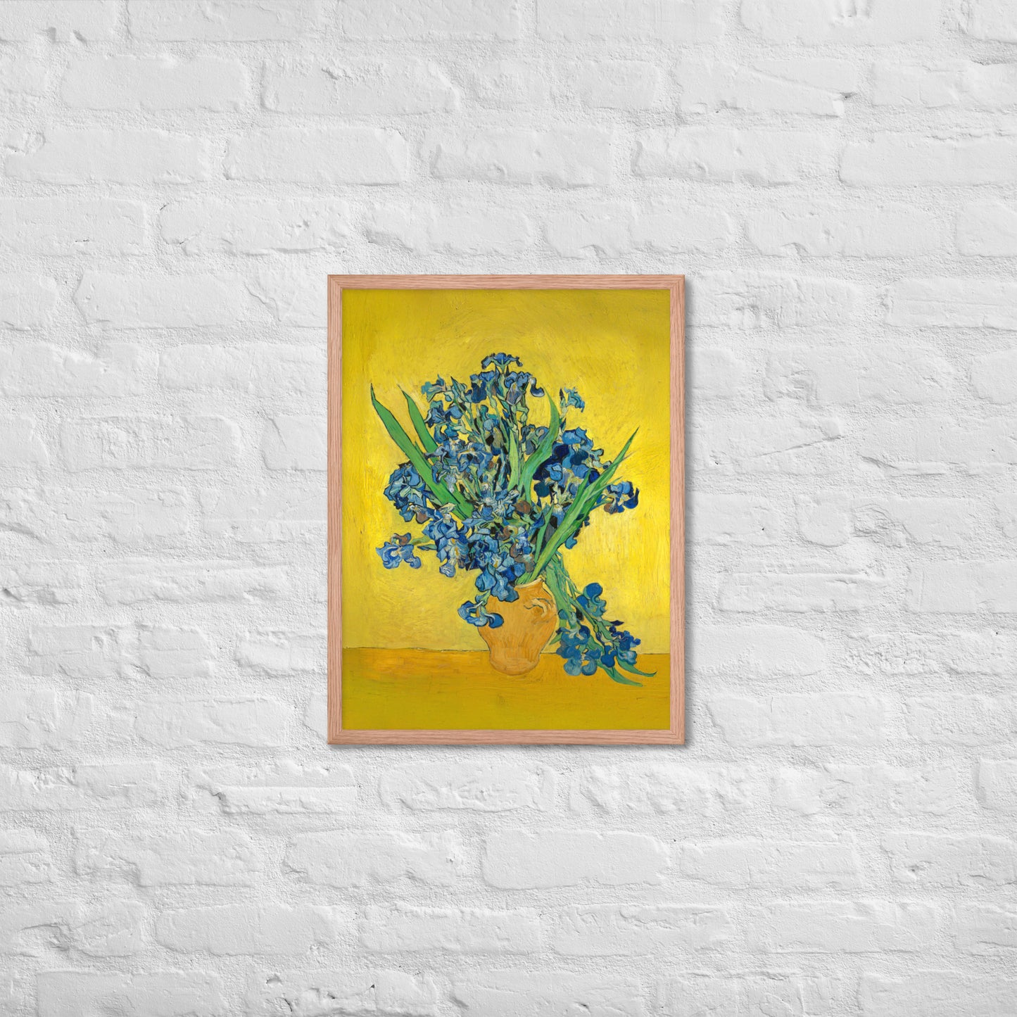 Van Gogh's 'Vase with Irises Against a Yellow Background' on a 18"x24" red oak framed poster print on a white brick wall.