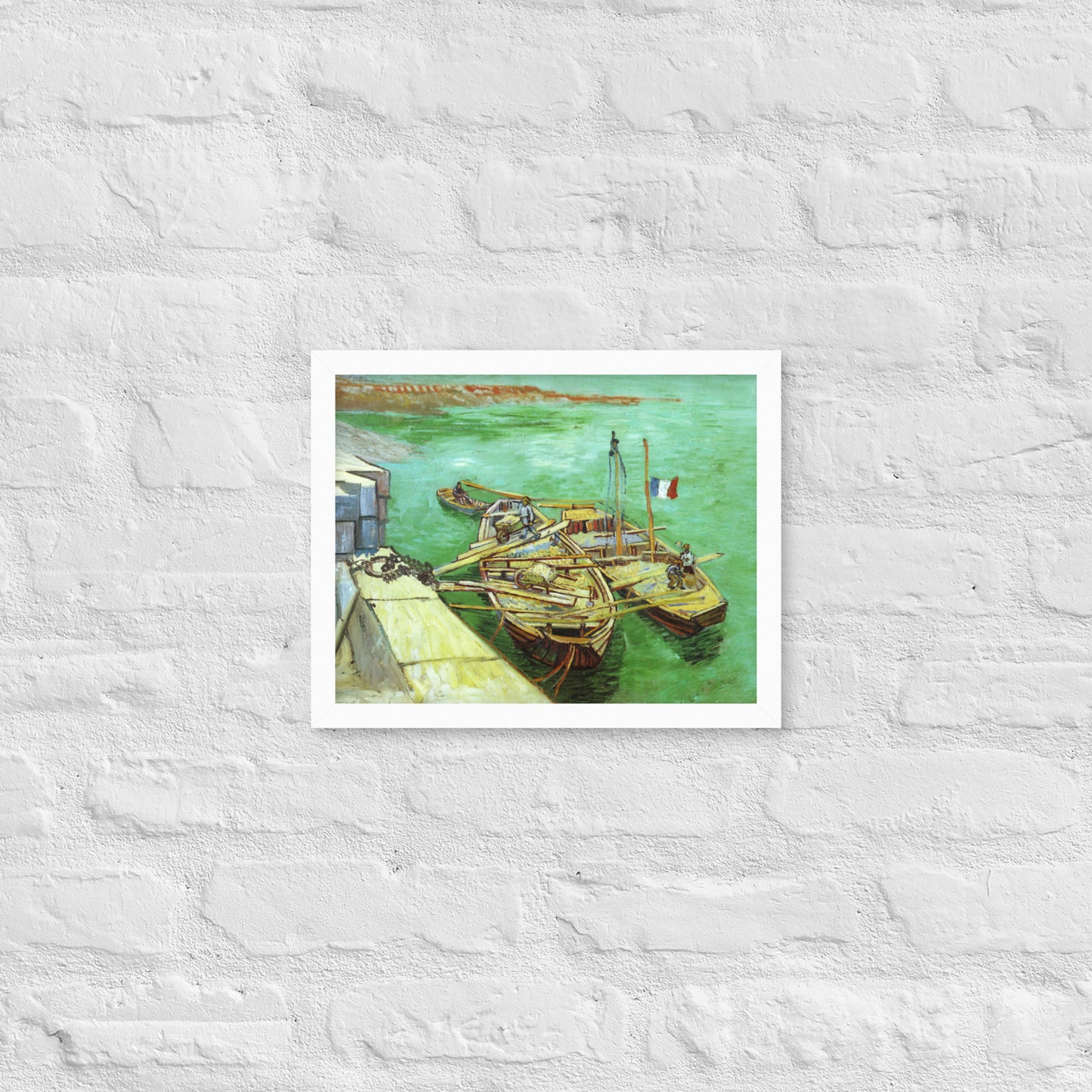 Van Gogh's 'Quay with Men Unloading Sand Barges' on a 11"x14" white framed poster print on a white brick wall.
