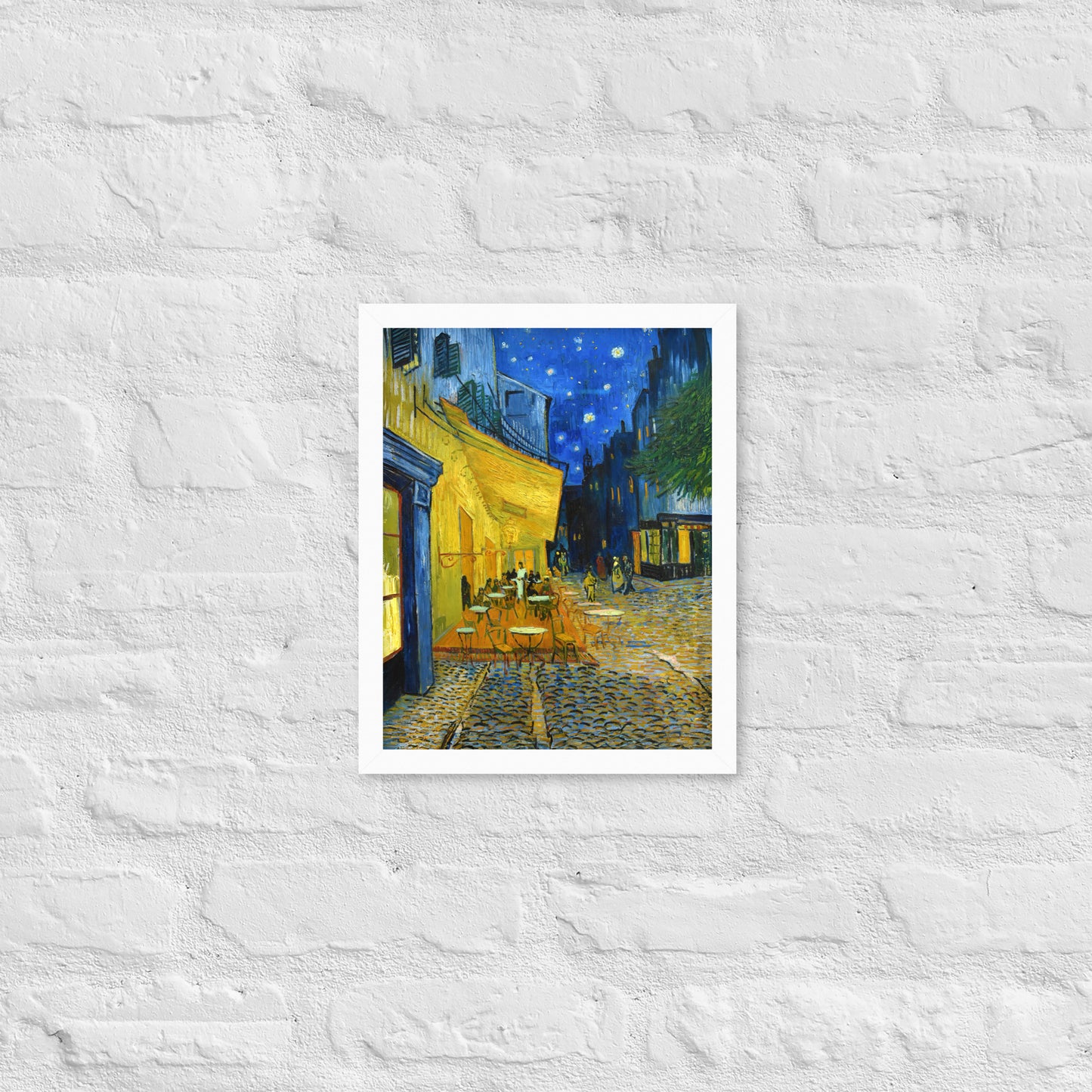 Van Gogh's 'Café Terrace at Night' on a 11"x14" white framed poster print on a white brick wall.