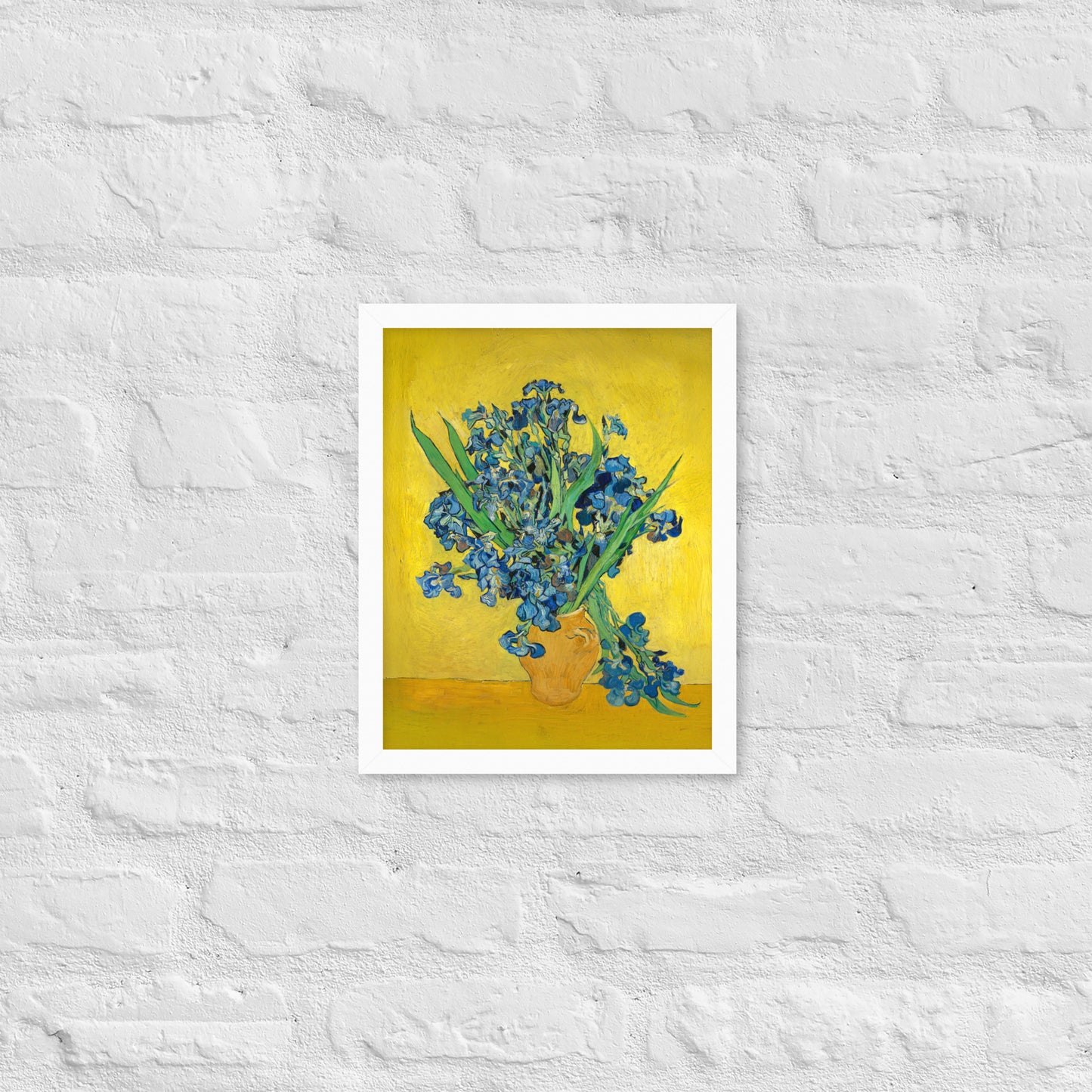 Van Gogh's 'Vase with Irises Against a Yellow Background' on a 11"x14" white framed poster print on a white brick wall.