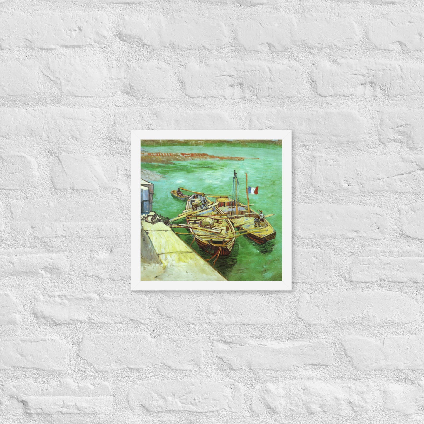 Van Gogh's 'Quay with Men Unloading Sand Barges' on a 12"x12" white framed poster print on a white brick wall.