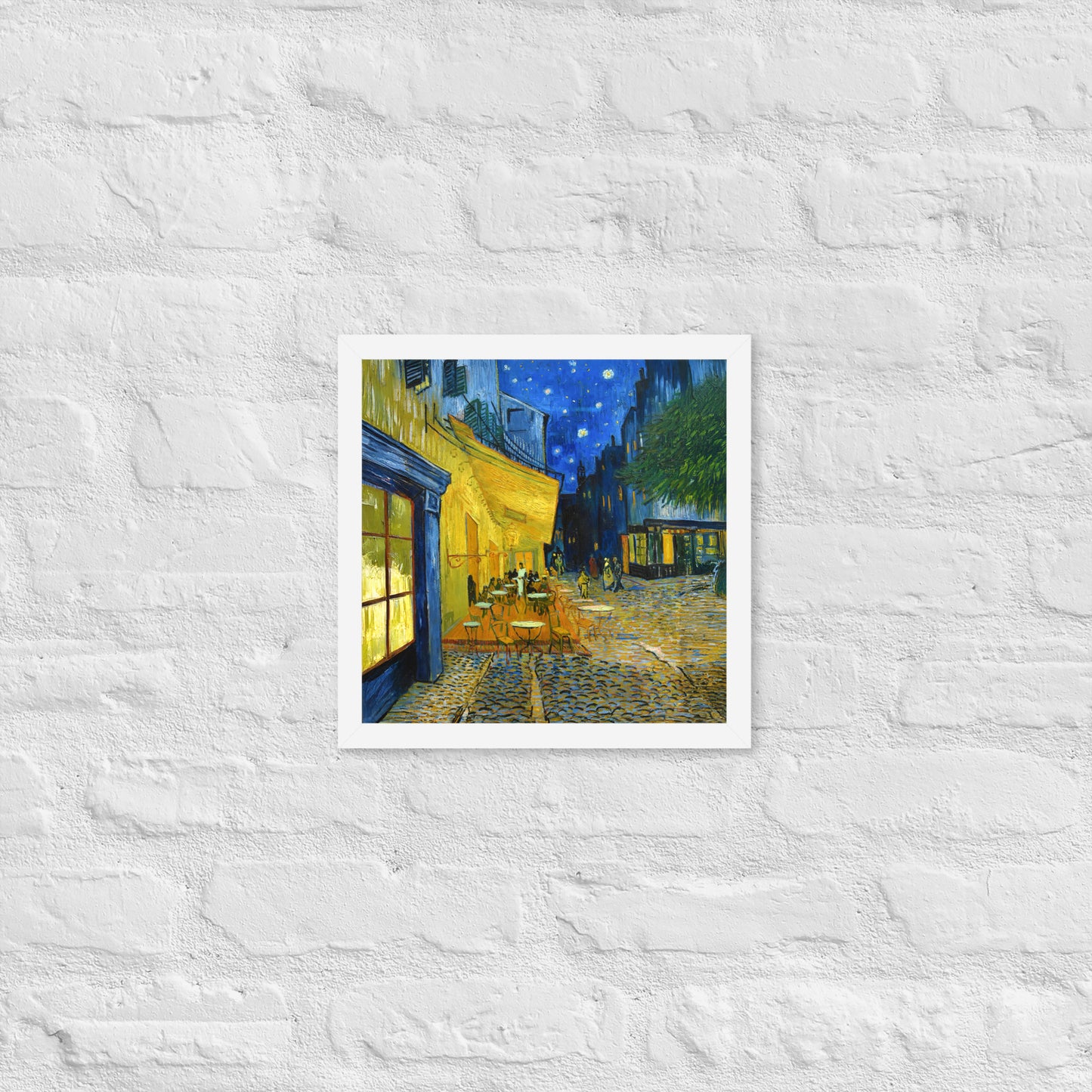 Van Gogh's 'Café Terrace at Night' on a 12"x12" white framed poster print on a white brick wall.