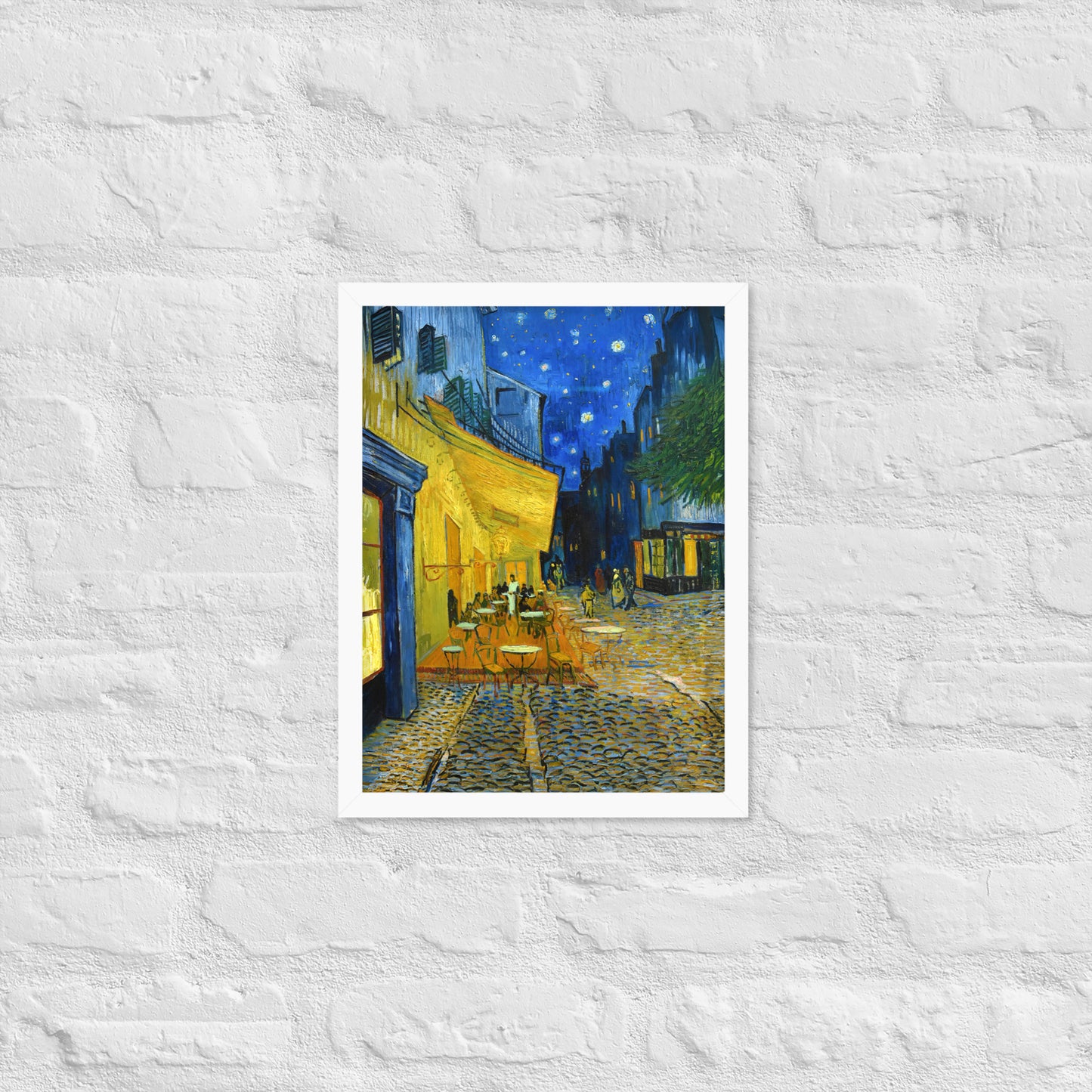 Van Gogh's 'Café Terrace at Night' on a 12"x16" white framed poster print on a white brick wall.