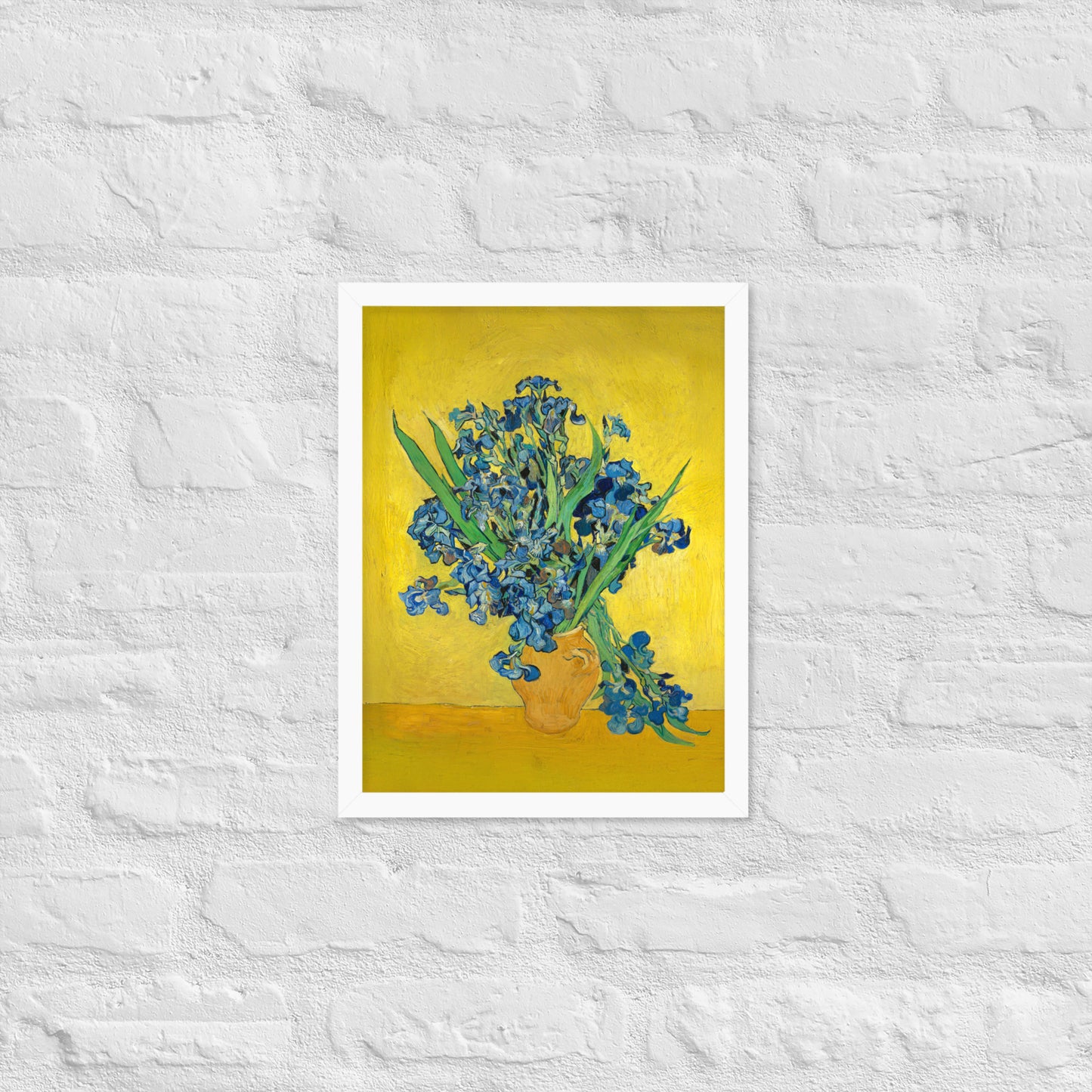 Van Gogh's 'Vase with Irises Against a Yellow Background' on a 12"x16" white framed poster print on a white brick wall.