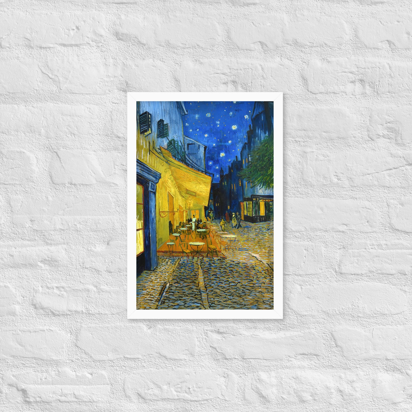 Van Gogh's 'Café Terrace at Night' on a 12"x18" white framed poster print on a white brick wall.
