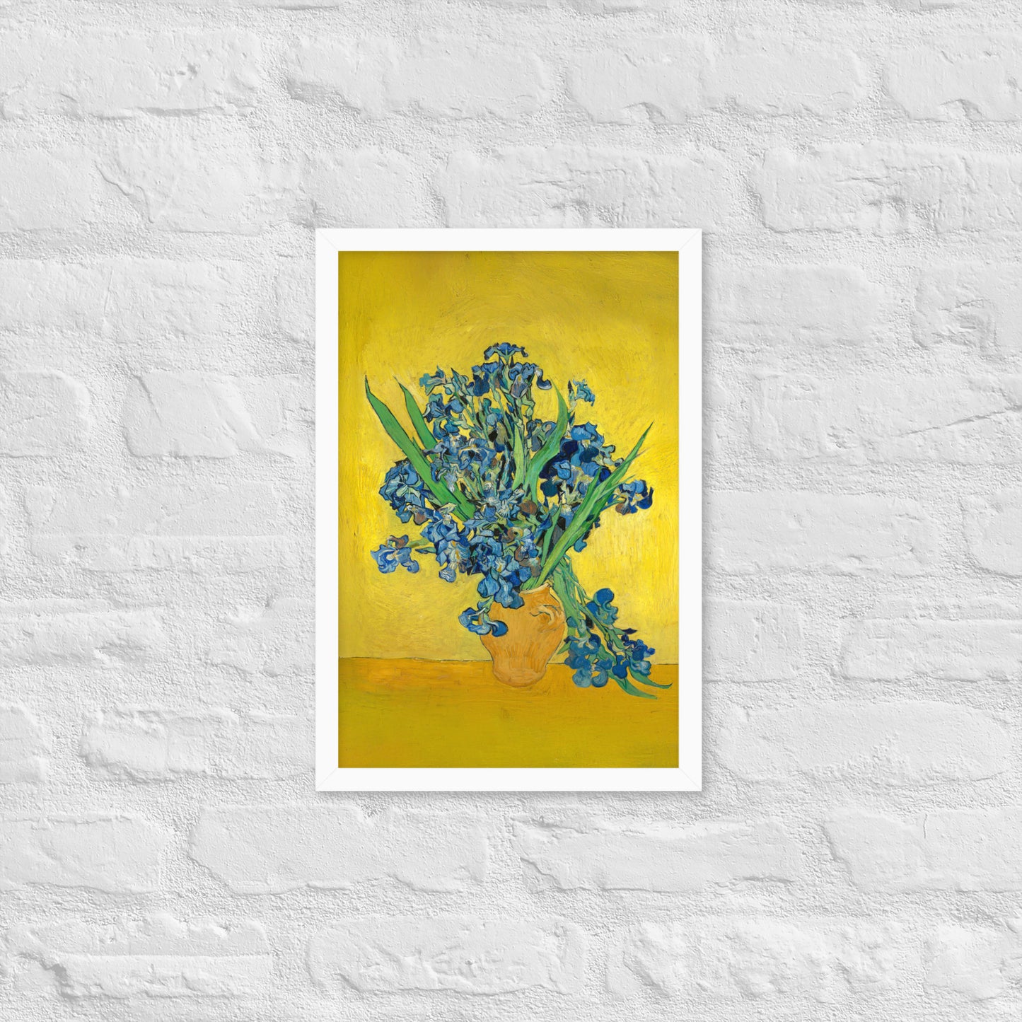 Van Gogh's 'Vase with Irises Against a Yellow Background' on a 12"x18" white framed poster print on a white brick wall.