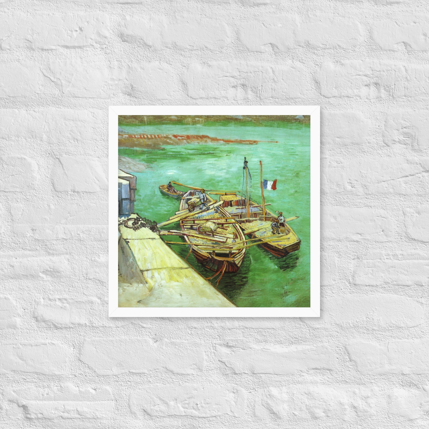 Van Gogh's 'Quay with Men Unloading Sand Barges' on a 16"x16" white framed poster print on a white brick wall.