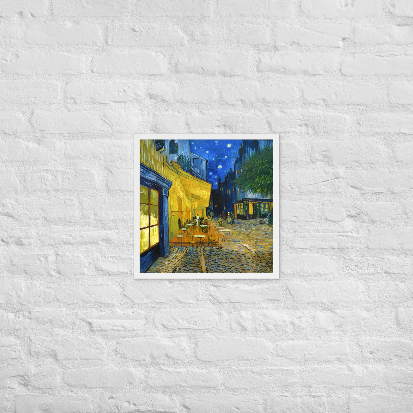 Van Gogh's 'Café Terrace at Night' on a 18"x18" white framed poster print on a white brick wall.