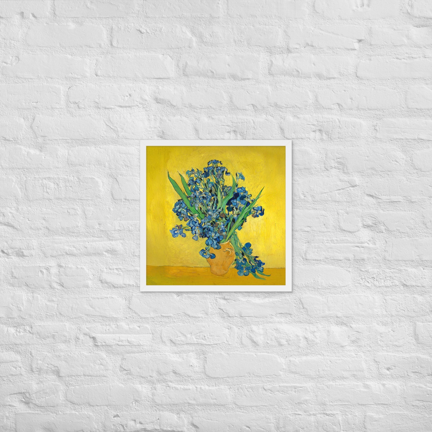 Van Gogh's 'Vase with Irises Against a Yellow Background' on a 18"x18" white framed poster print on a white brick wall.