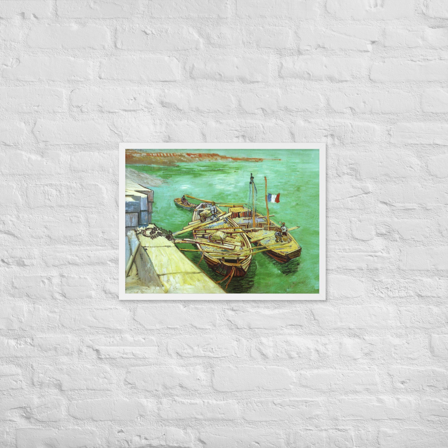 Van Gogh's 'Quay with Men Unloading Sand Barges' on a 18"x24" white framed poster print on a white brick wall.