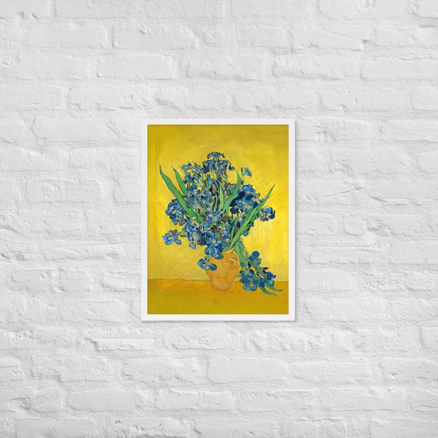 Van Gogh's 'Vase with Irises Against a Yellow Background' on a 18"x24" white framed poster print on a white brick wall.