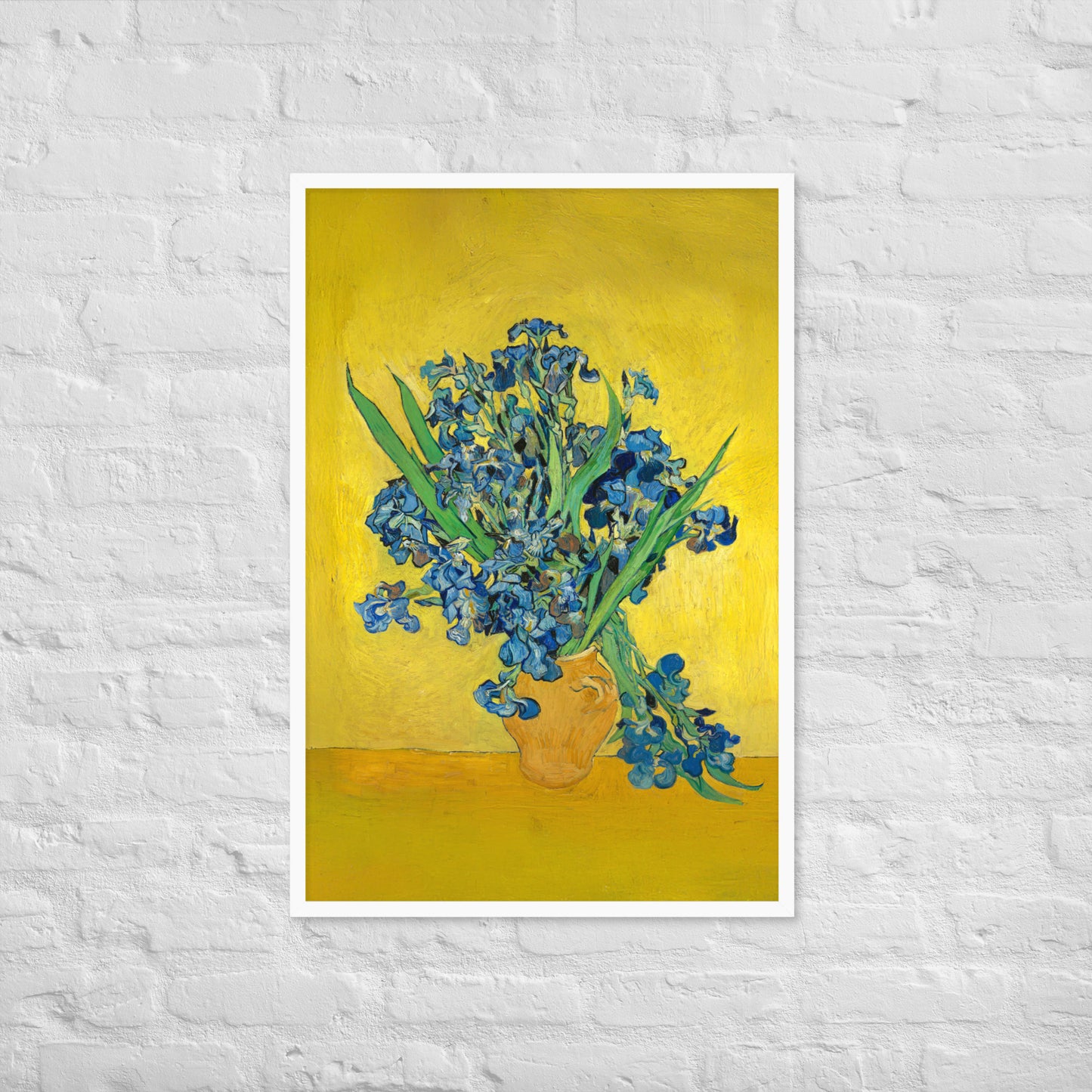 Van Gogh's 'Vase with Irises Against a Yellow Background' on a 24"x36" white framed poster print on a white brick wall.