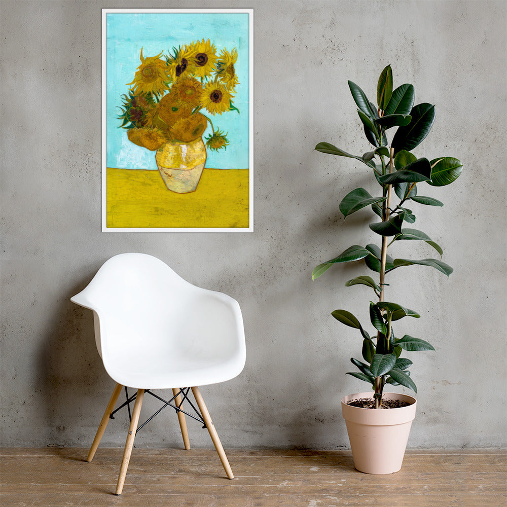 Van Gogh's 'Vase with Twelve Sunflowers' on a 24"x36" white framed poster print on a light gray concrete wall with a white chair and plant below.