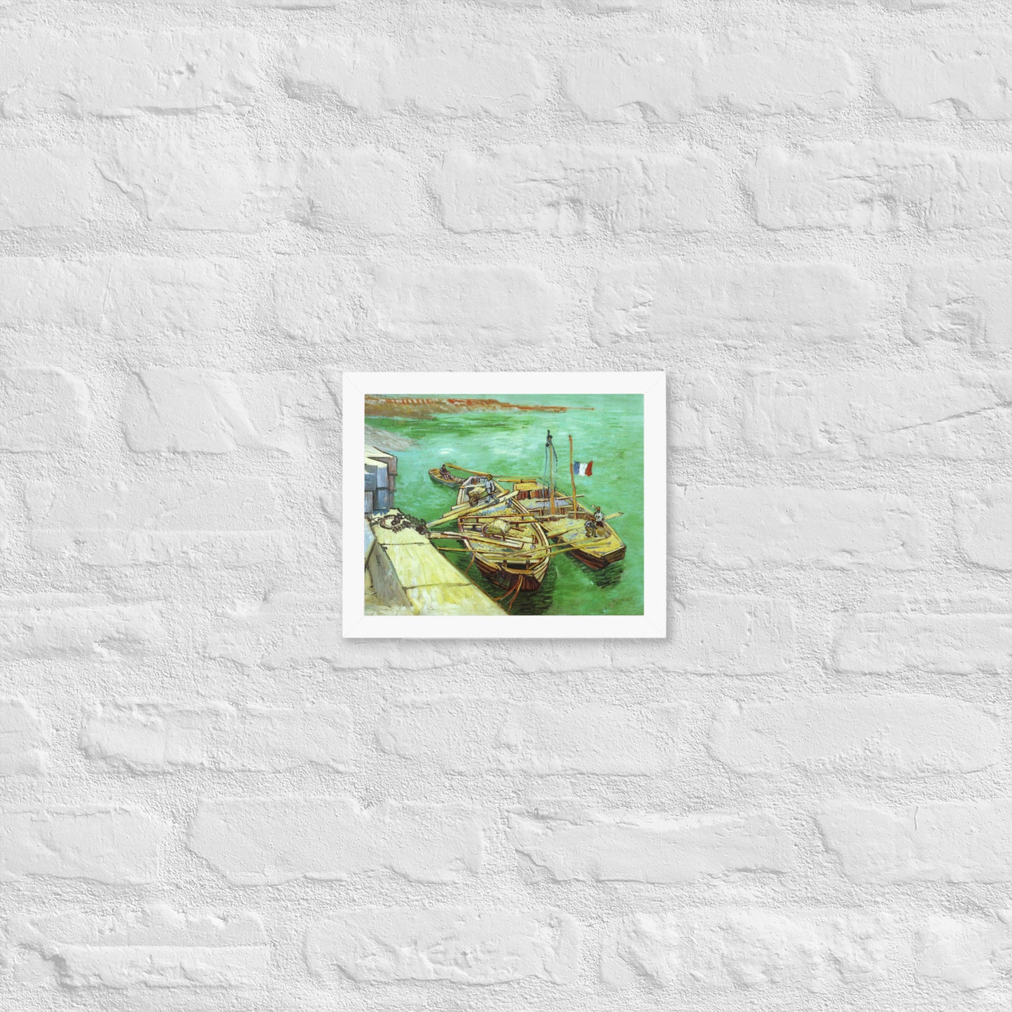 Van Gogh's 'Quay with Men Unloading Sand Barges' on a 8"x10" white framed poster print on a white brick wall.