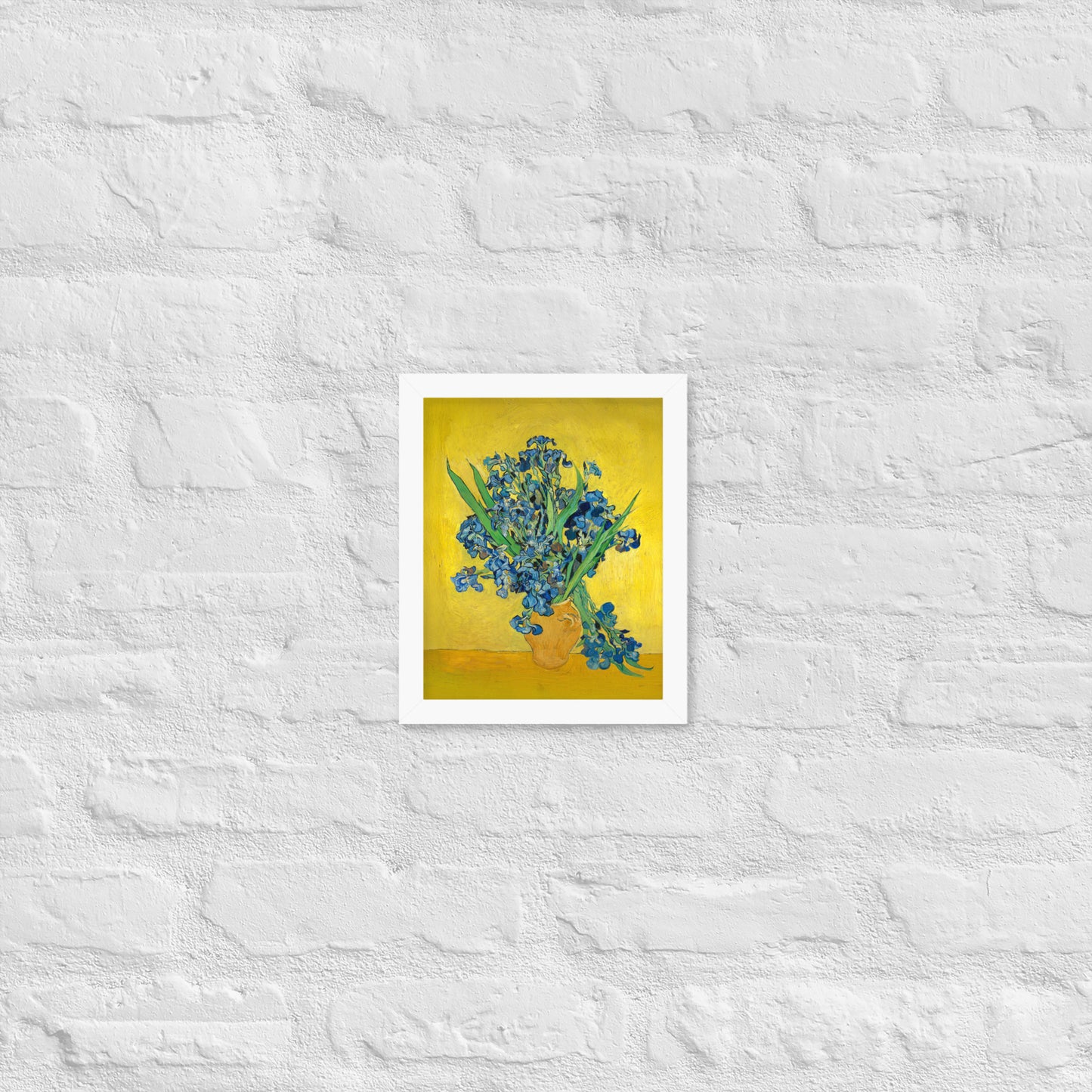 Van Gogh's 'Vase with Irises Against a Yellow Background' on a 8"x10" white framed poster print on a white brick wall.