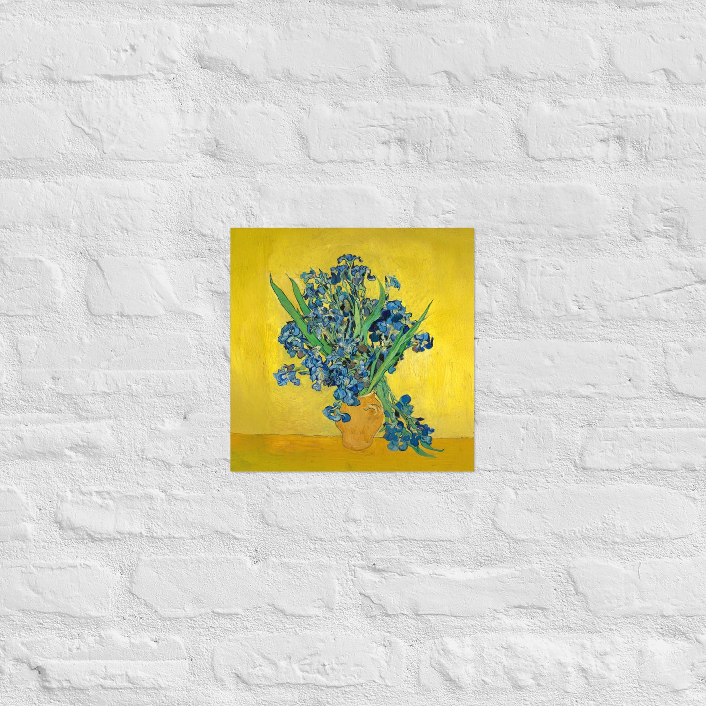 Van Gogh's 'Vase with Irises Against a Yellow Background' on a 12"x12" unframed poster print on a white brick wall.