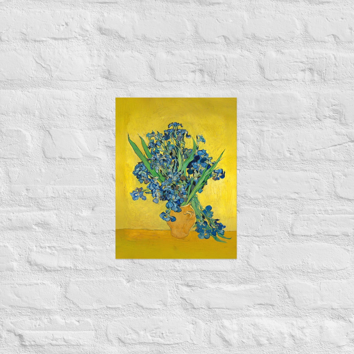 Van Gogh's 'Vase with Irises Against a Yellow Background' on a 12"x16" unframed poster print on a white brick wall.