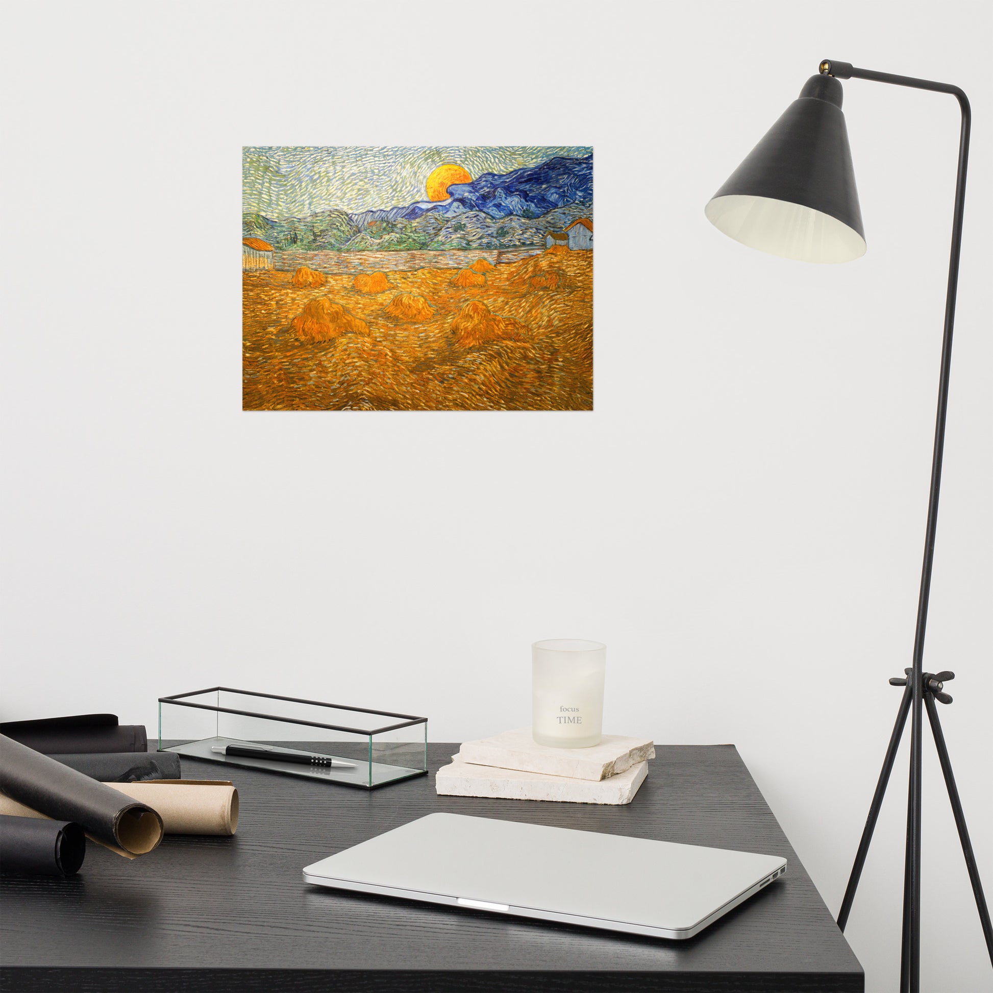 Van Gogh's 'Landscape with Wheat Sheaves and Rising Moon' on a 12"x16" unframed poster print on a white wall above a modern office desk, lamp, and assorted desk items.