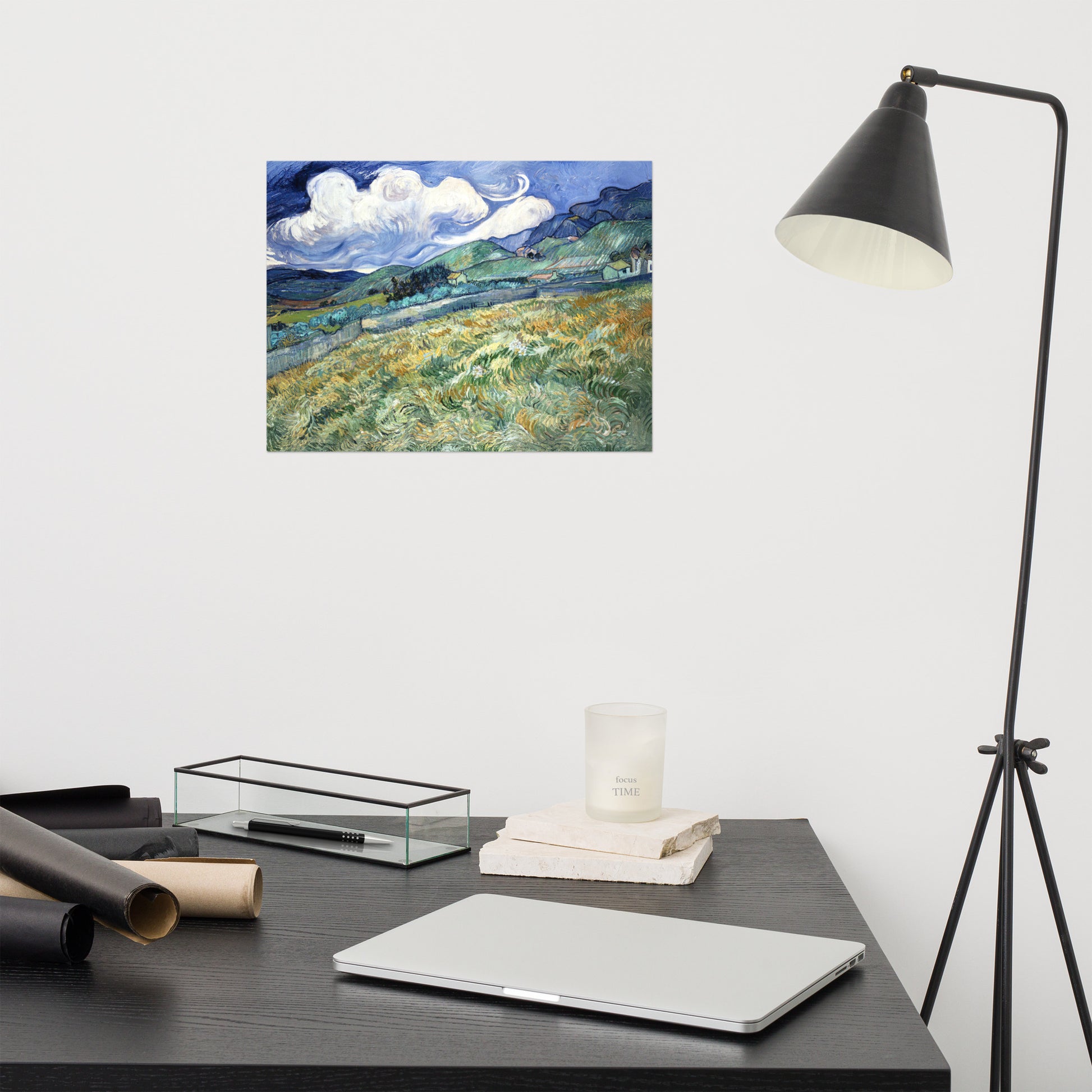 Van Gogh's 'Landscape from Saint-Rémy' on a 12"x16" unframed poster print on a white wall above a modern office desk, lamp, and assorted desk items.