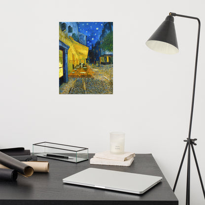 Van Gogh's 'Café Terrace at Night' on a 12"x16" unframed poster print on a white wall above a modern office desk, lamp, and assorted desk items.