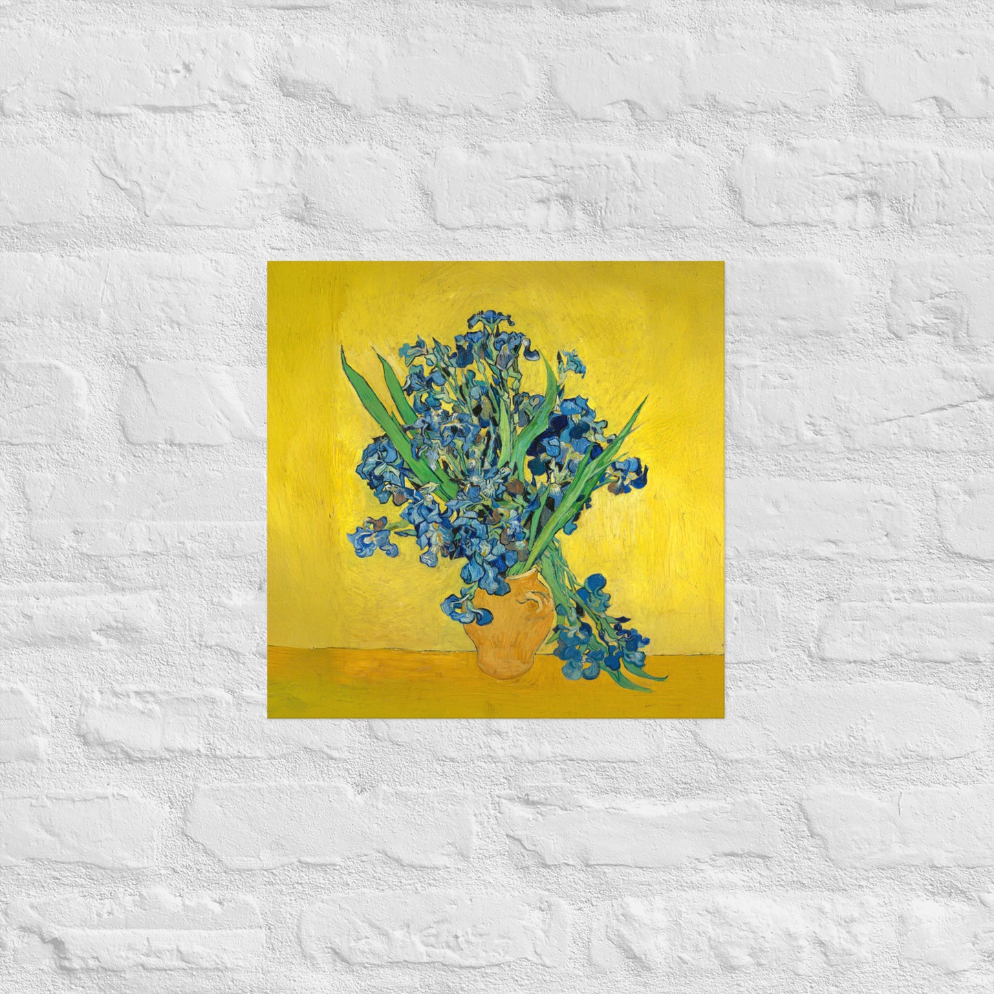 Van Gogh's 'Vase with Irises Against a Yellow Background' on a 16"x16" unframed poster print on a white brick wall.