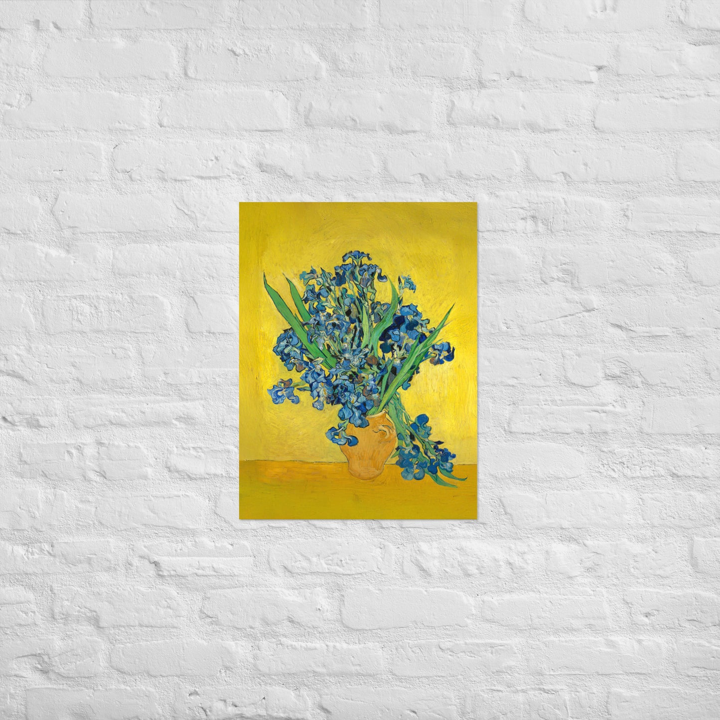 Van Gogh's 'Vase with Irises Against a Yellow Background' on a 18"x24" unframed poster print on a white brick wall.
