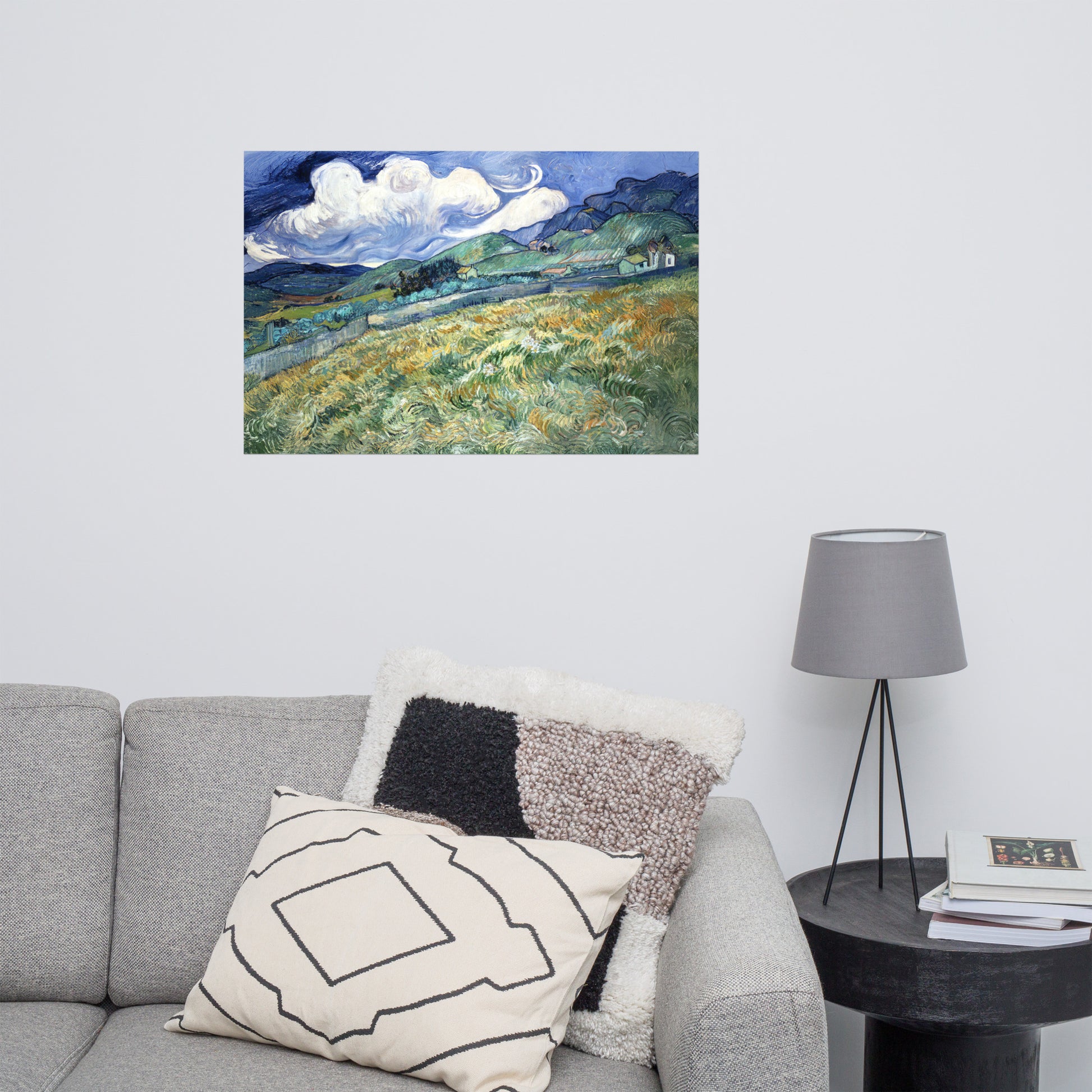 Van Gogh's 'Landscape from Saint-Rémy' on a 24"x36" unframed poster print on a white wall above a gray sofa with throw pillows and side table with a lamp.