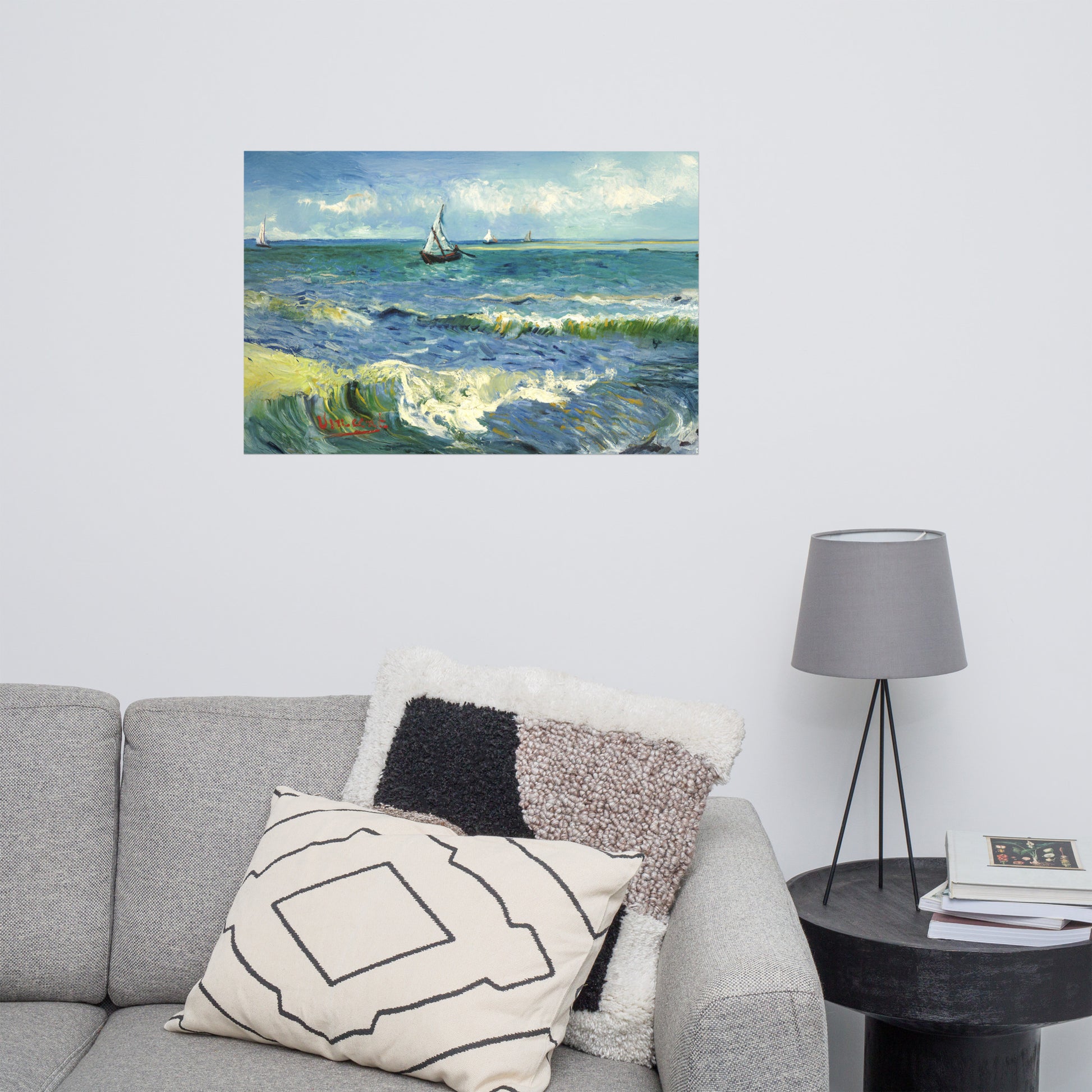 Van Gogh's 'The Sea at Les Saintes-Maries-de-la-Mer' on a 24"x36" unframed poster print on a white wall above a gray sofa with throw pillows and side table with a lamp.