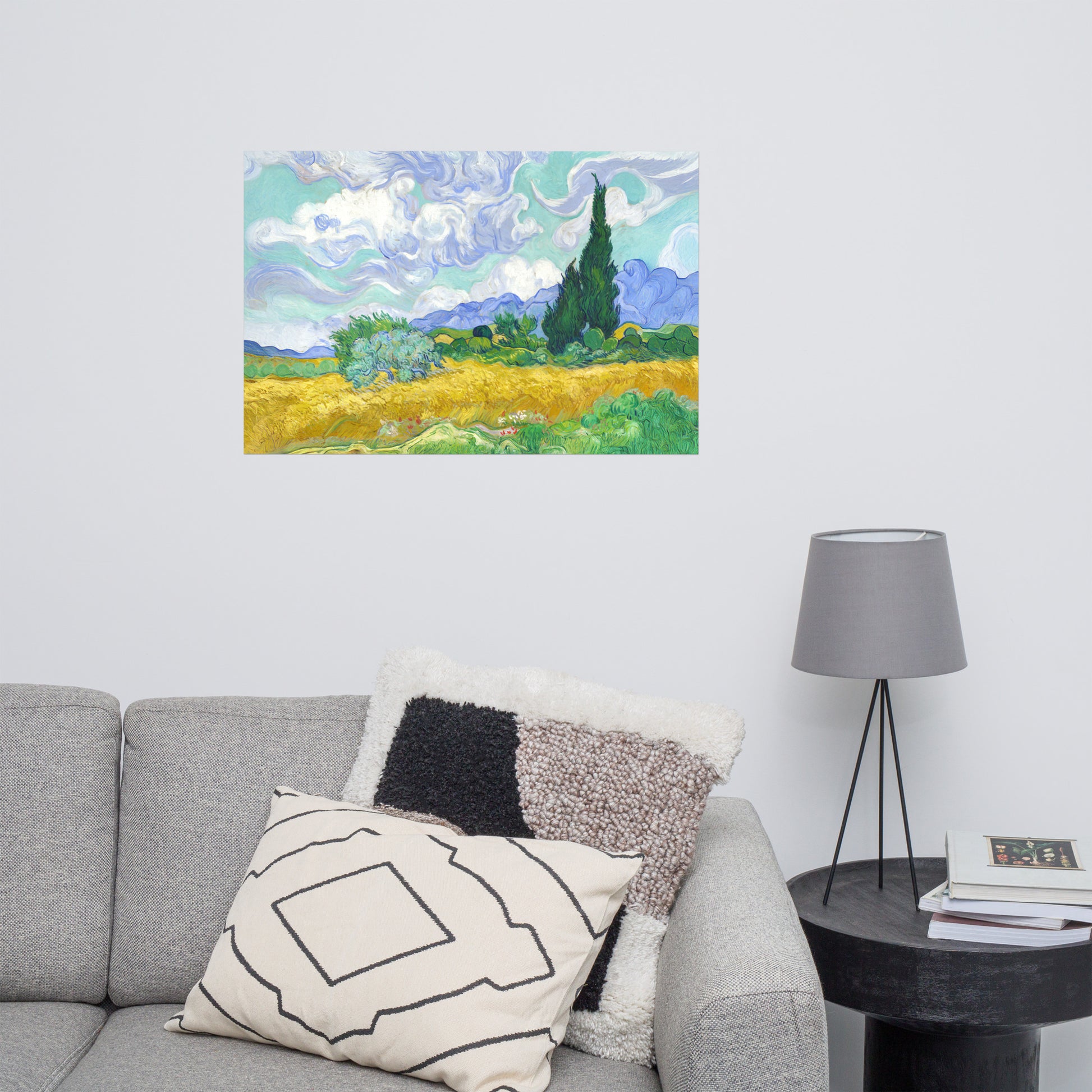 Van Gogh's 'Wheat Field with Cypresses' on a 24"x36" unframed poster print on a white wall above a gray sofa with throw pillows and side table with a lamp.