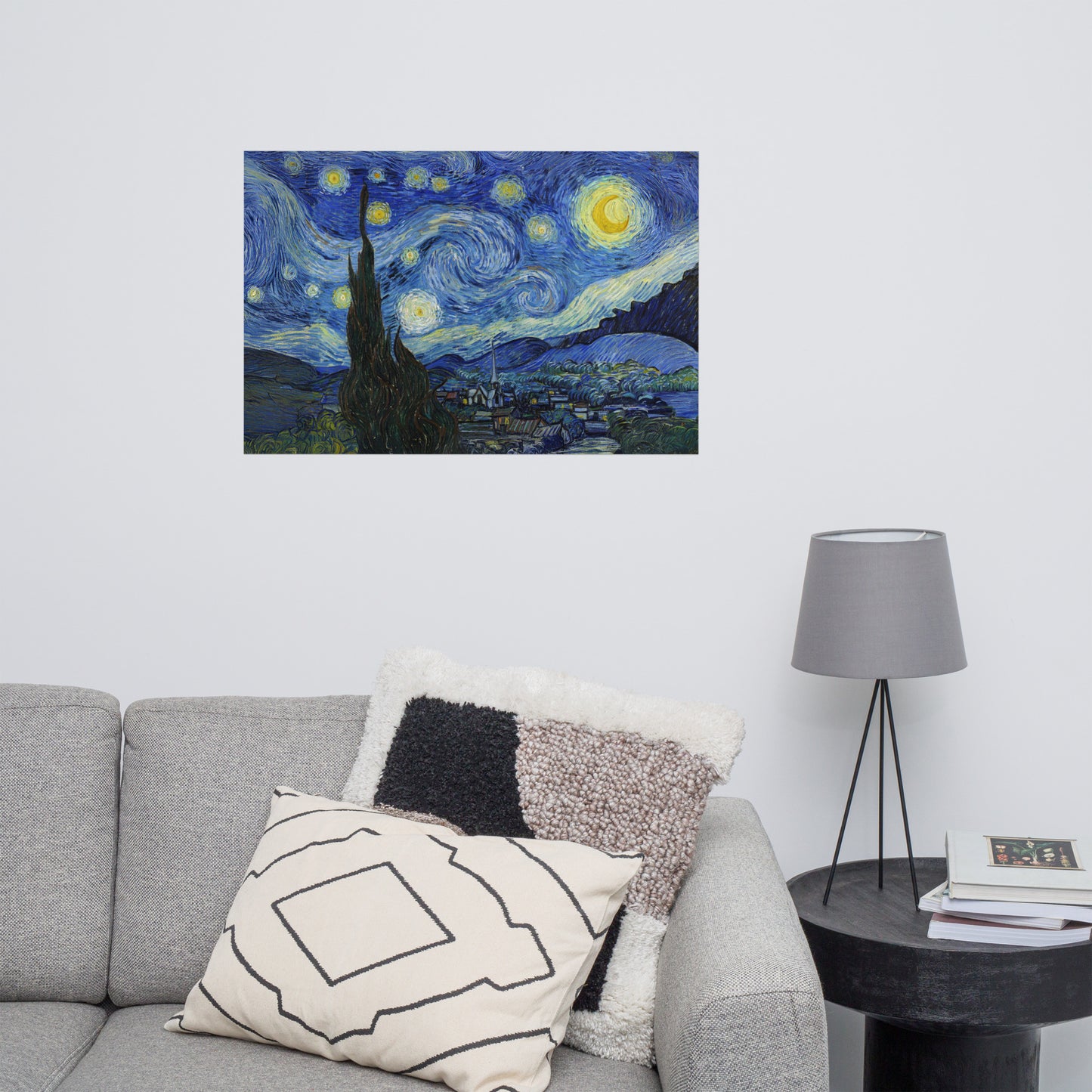 Van Gogh's 'Starry Night' on a 24"x36" unframed poster print on a white wall above a gray sofa with throw pillows and side table with a lamp.