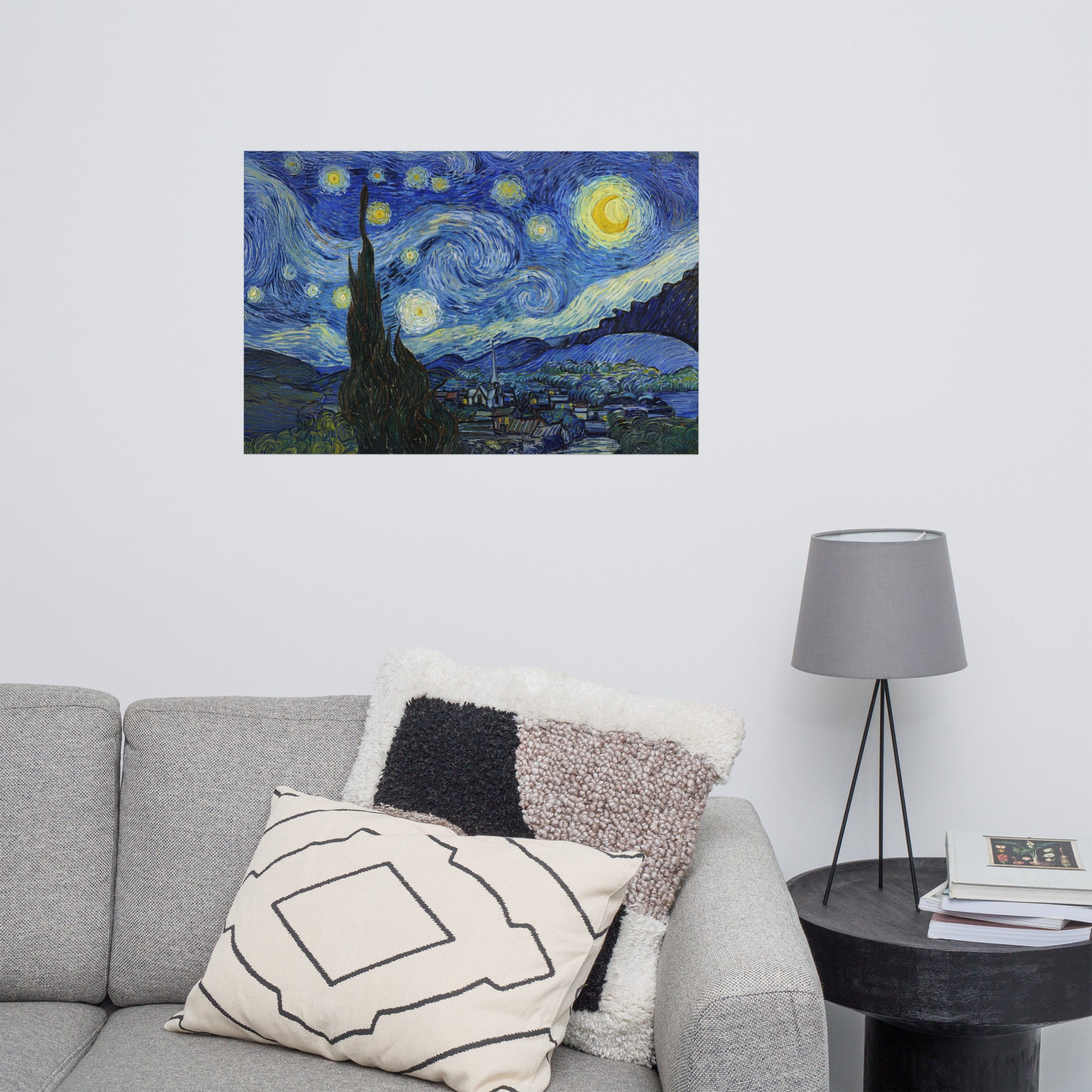 Van Gogh's 'Starry Night' on a 24"x36" unframed poster print on a white wall above a gray sofa with throw pillows and side table with a lamp.