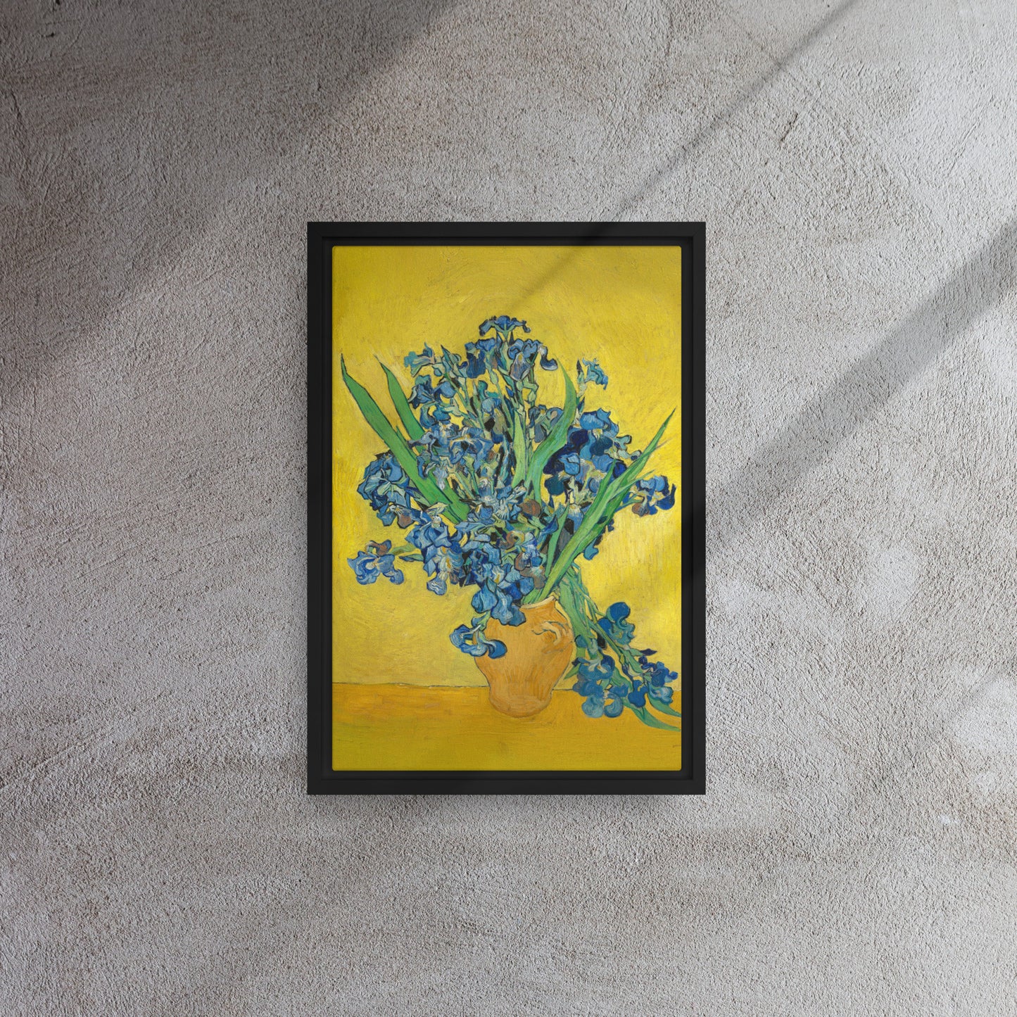 Van Gogh's 'Vase with Irises Against a Yellow Background' on a 12"x18" black framed canvas print on a textured gray wall.