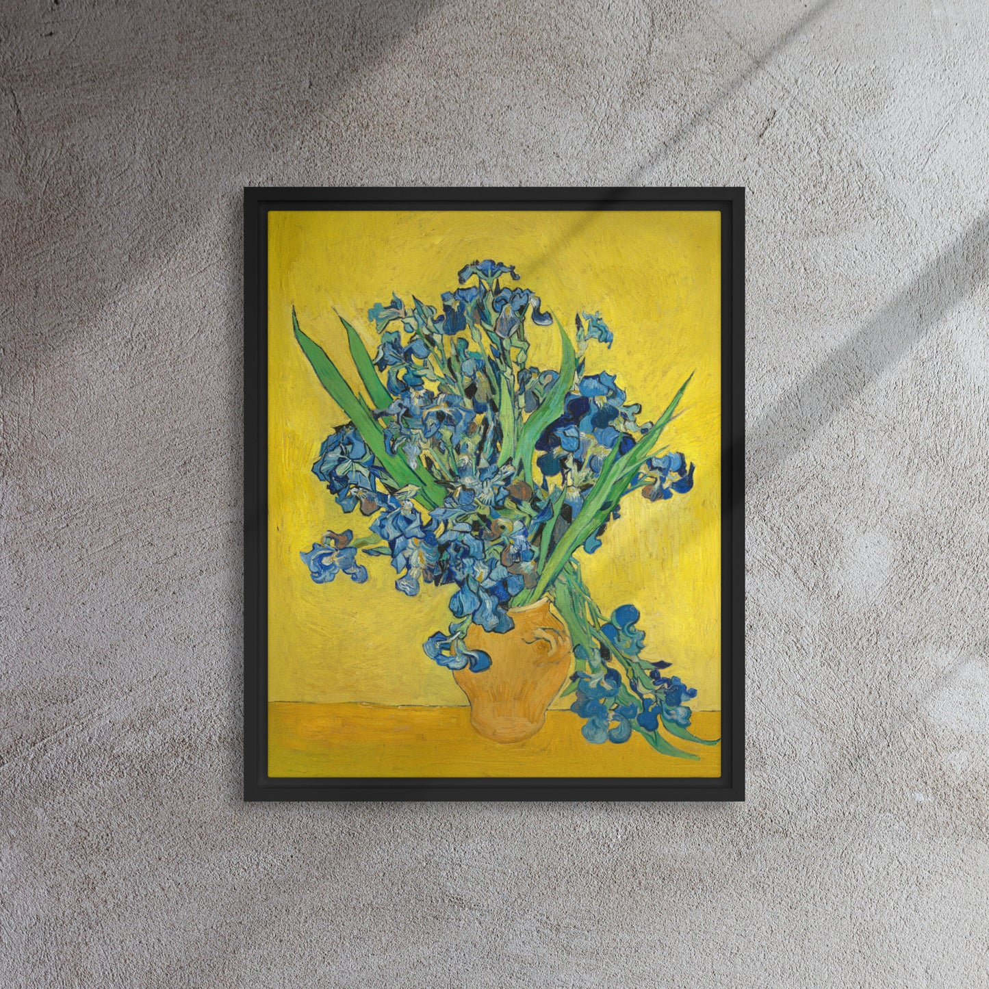 Van Gogh's 'Vase with Irises Against a Yellow Background' on a 16"x20" black framed canvas print on a textured gray wall.