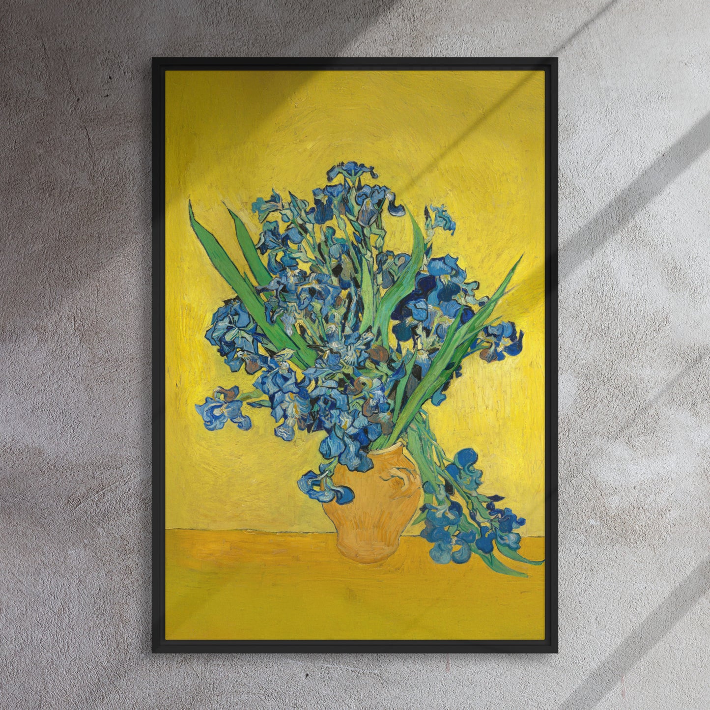 Van Gogh's 'Vase with Irises Against a Yellow Background' on a 24"x36" black framed canvas print on a textured gray wall.
