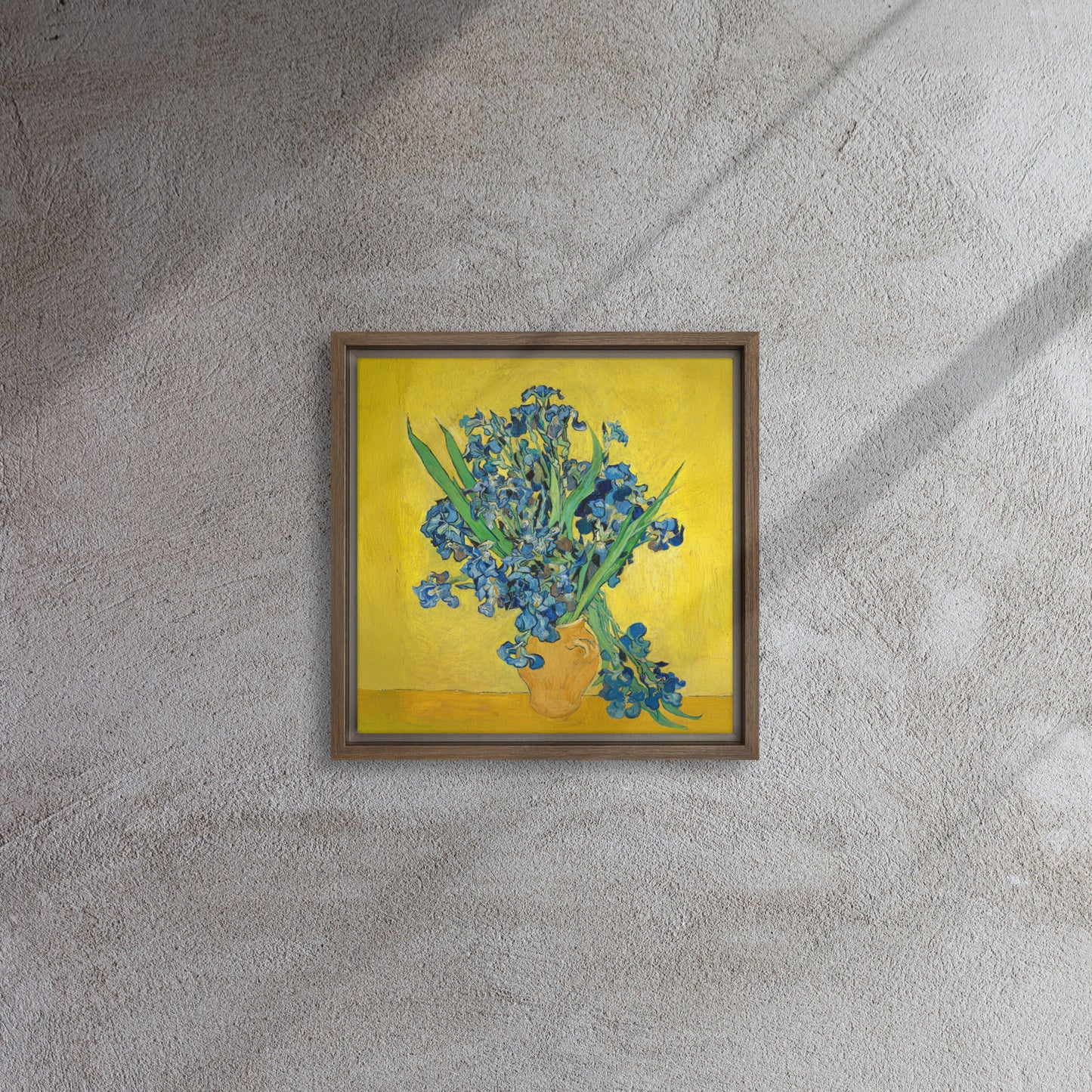 Van Gogh's 'Vase with Irises Against a Yellow Background' on a 12"x12" brown framed canvas print on a textured gray wall.