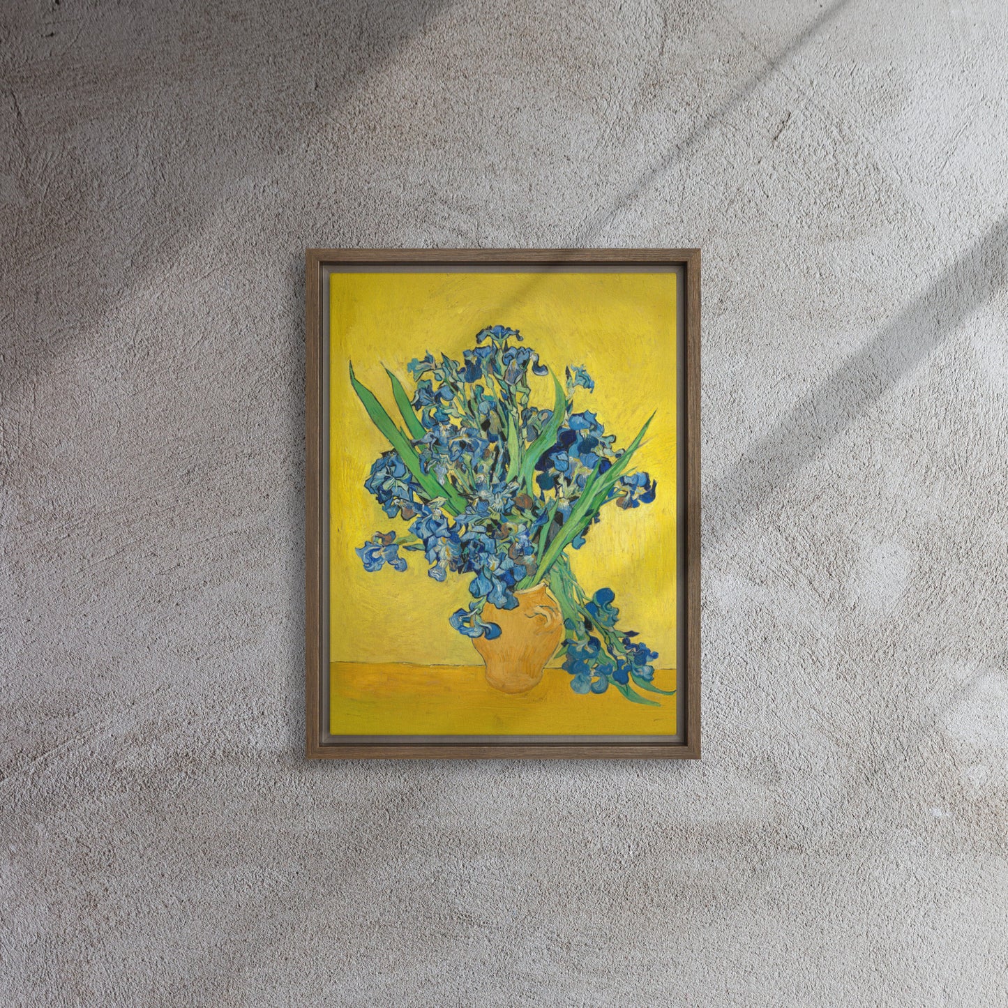 Van Gogh's 'Vase with Irises Against a Yellow Background' on a 12"x16" brown framed canvas print on a textured gray wall.