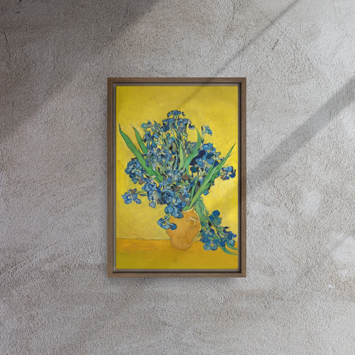 Van Gogh's 'Vase with Irises Against a Yellow Background' on a 12"x18" brown framed canvas print on a textured gray wall.