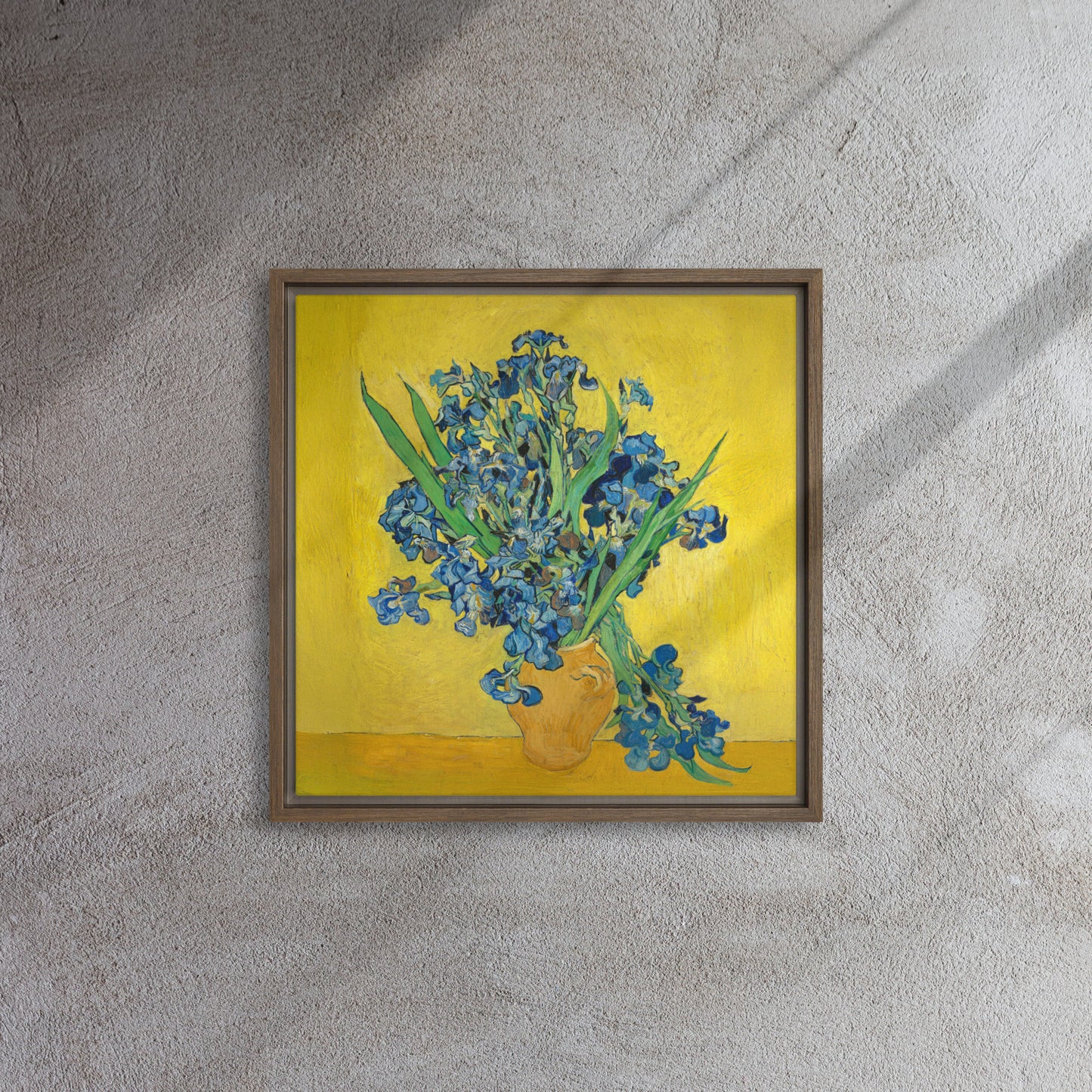 Van Gogh's 'Vase with Irises Against a Yellow Background' on a 16"x16" brown framed canvas print on a textured gray wall.