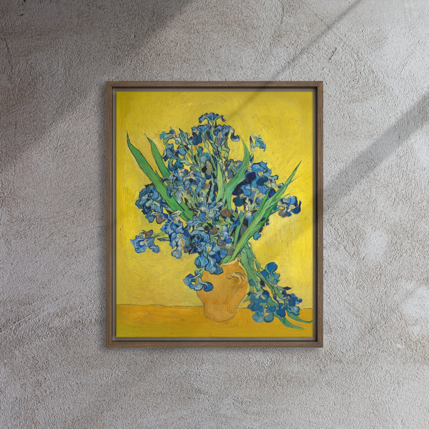 Van Gogh's 'Vase with Irises Against a Yellow Background' on a 16"x20" brown framed canvas print on a textured gray wall.