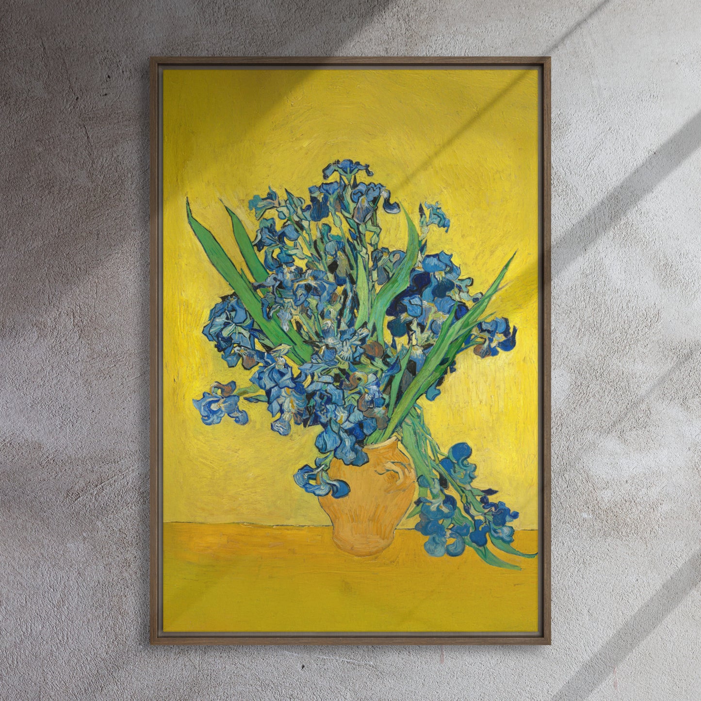 Van Gogh's 'Vase with Irises Against a Yellow Background' on a 24"x36" brown framed canvas print on a textured gray wall.