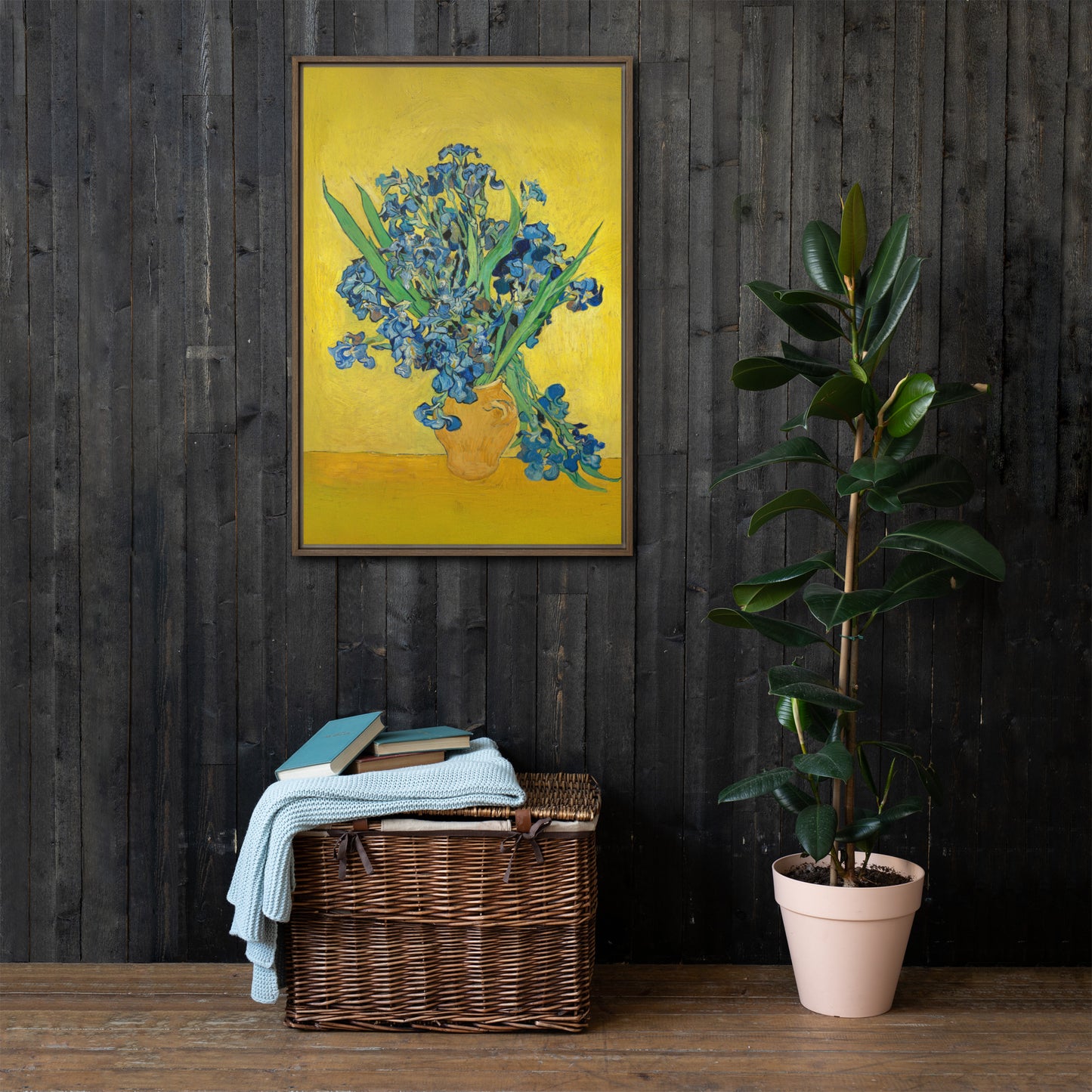 Van Gogh's 'Vase with Irises Against a Yellow Background' on a 24"x36" brown framed canvas print on a dark wooden wall with a wicker bin and plant below.