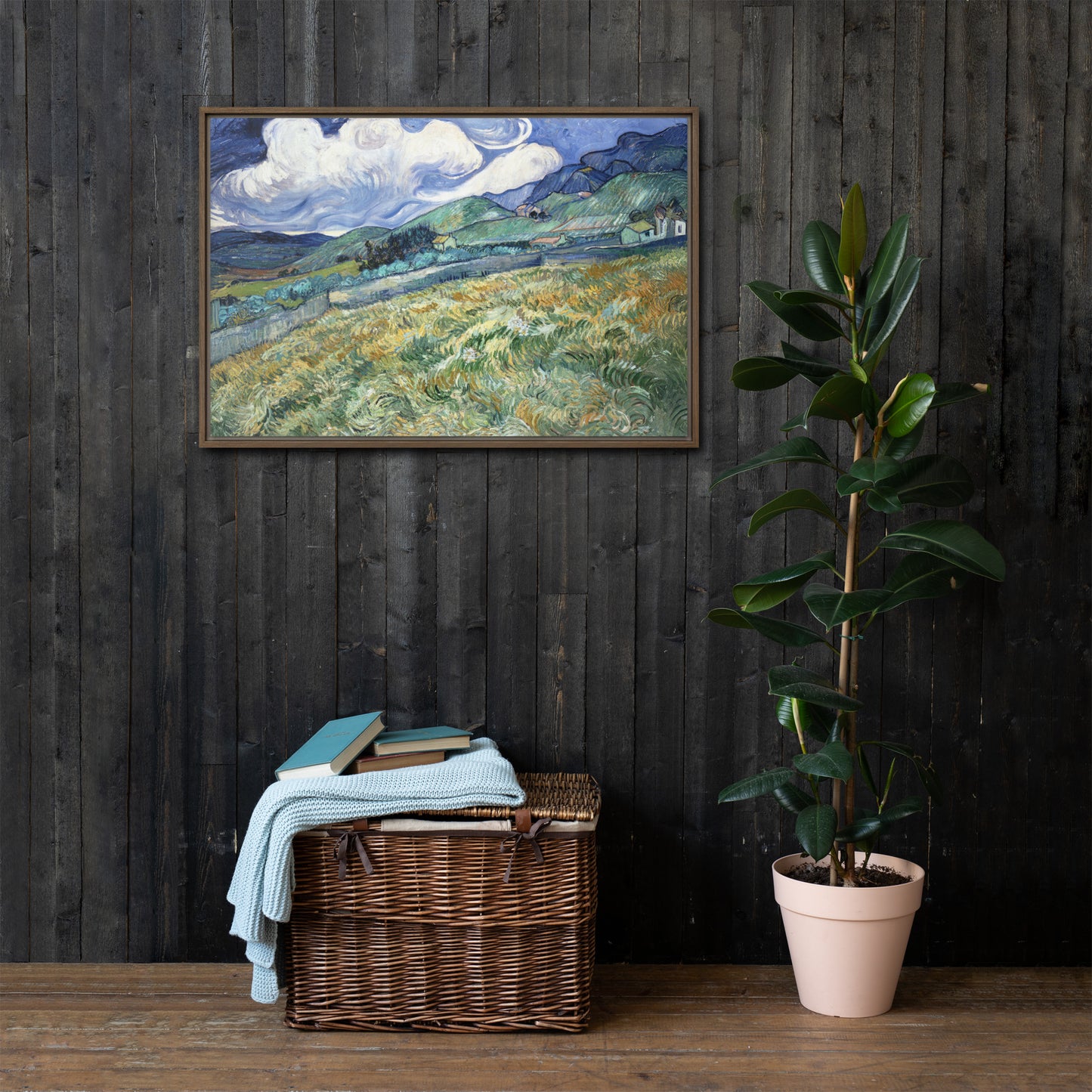 Van Gogh's 'Landscape from Saint-Rémy' on a 24"x36" brown framed canvas print on a dark wooden wall with a wicker bin and plant below.