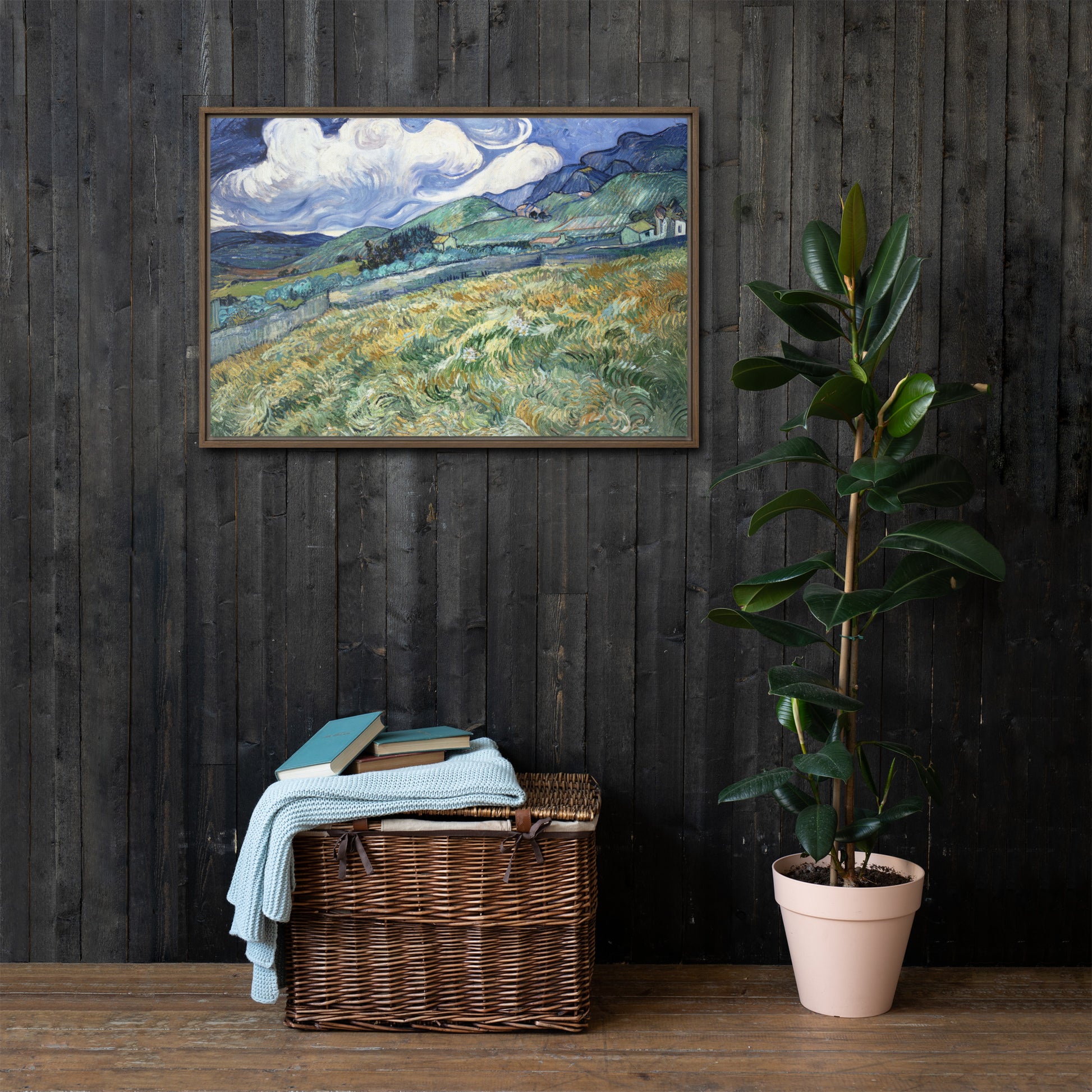 Van Gogh's 'Landscape from Saint-Rémy' on a 24"x36" brown framed canvas print on a dark wooden wall with a wicker bin and plant below.