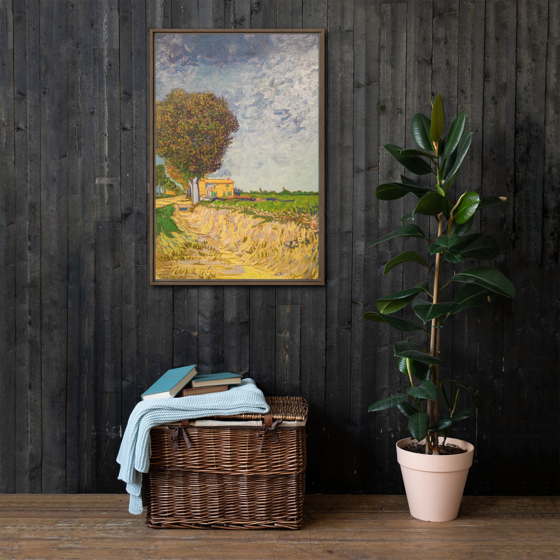 Van Gogh's 'A Lane near Arles' on a 24"x36" brown framed canvas print on a dark wooden wall with a wicker bin and plant below.