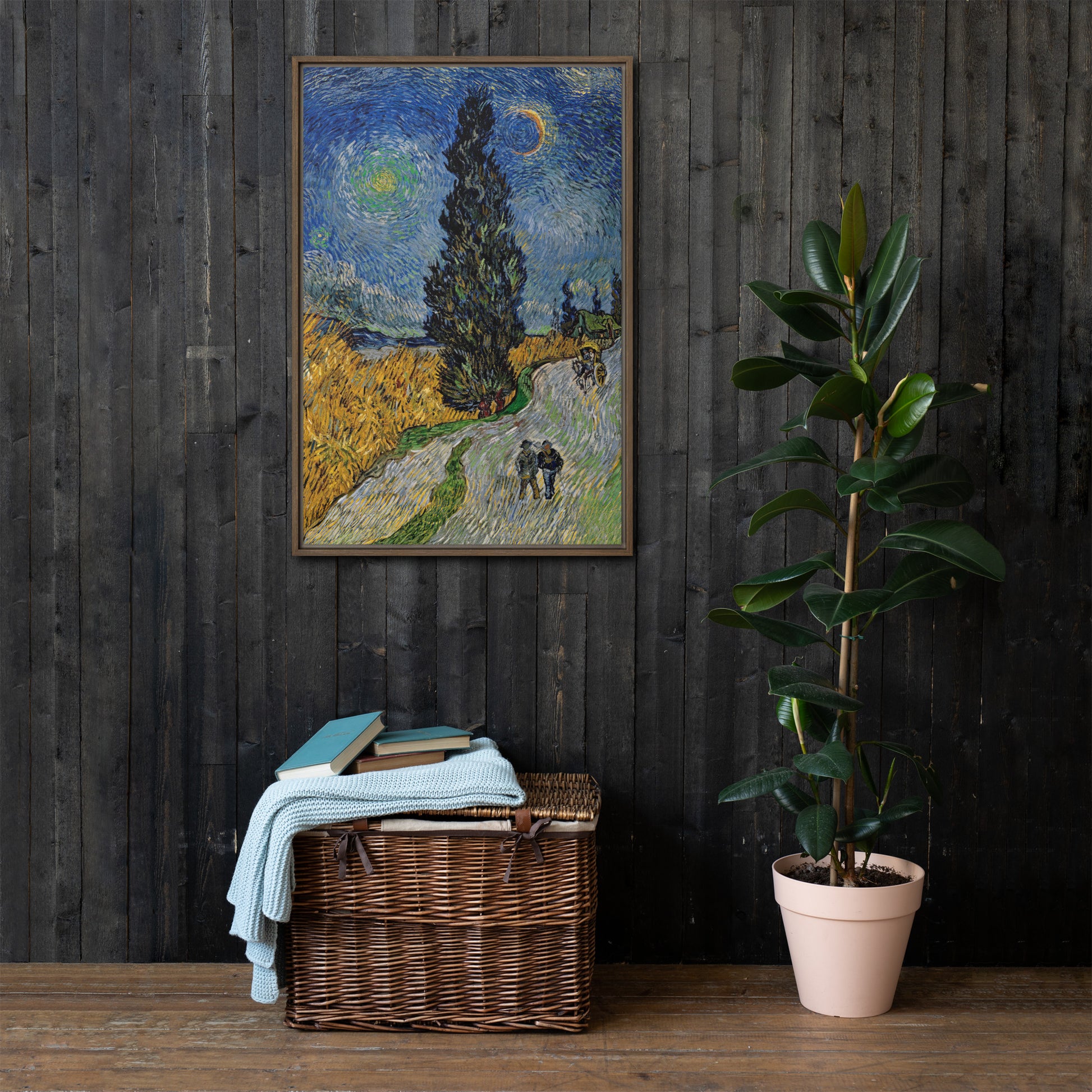 Van Gogh's 'Road with Cypress and Star' on a 24"x36" brown framed canvas print on a dark wooden wall with a wicker bin and plant below.