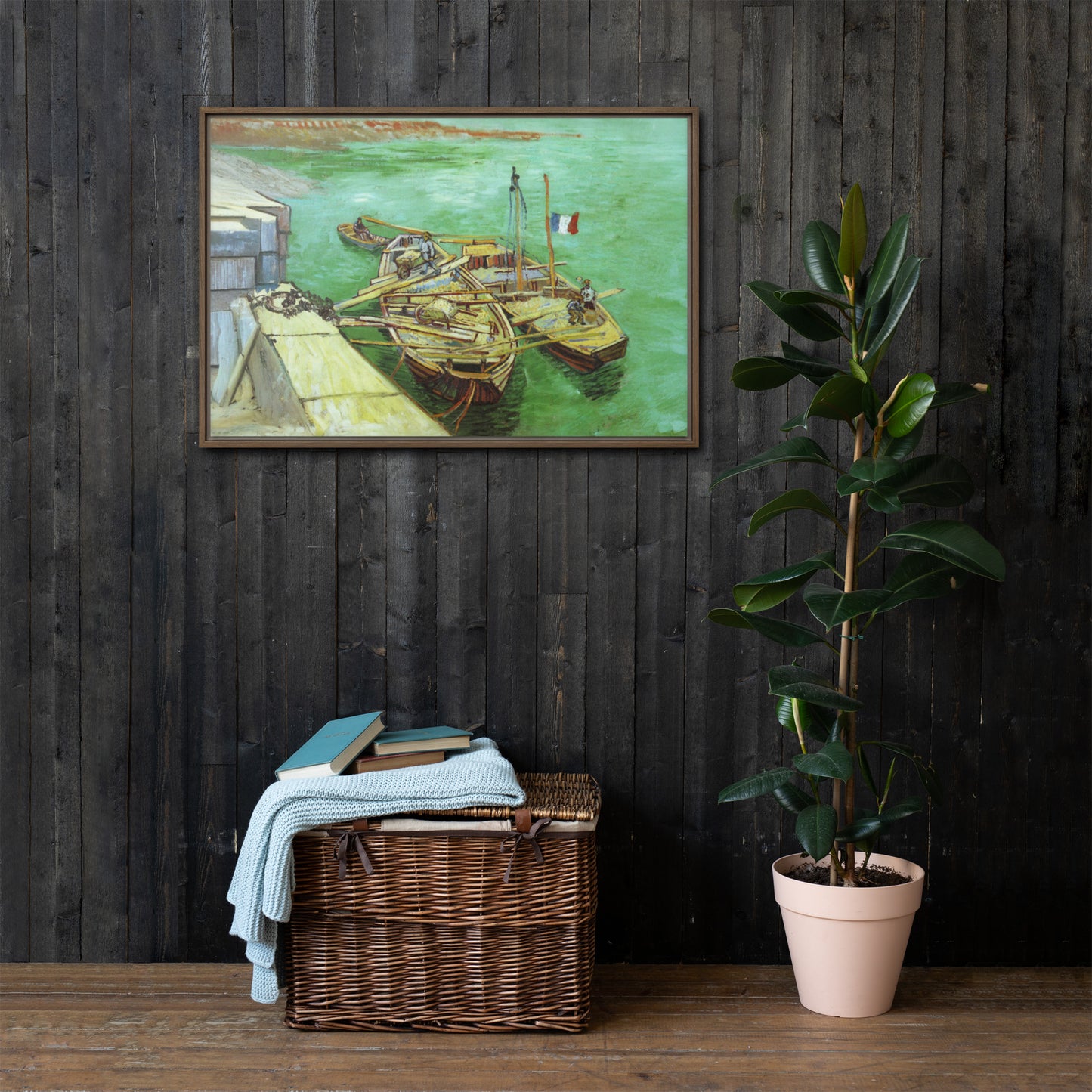 Van Gogh's 'Quay with Men Unloading Sand Barges' on a 24"x36" brown framed canvas print on a dark wooden wall with a wicker bin and plant below.