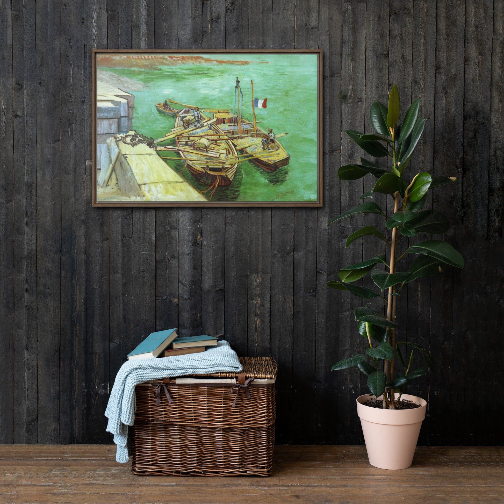 Van Gogh's 'Quay with Men Unloading Sand Barges' on a 24"x36" brown framed canvas print on a dark wooden wall with a wicker bin and plant below.
