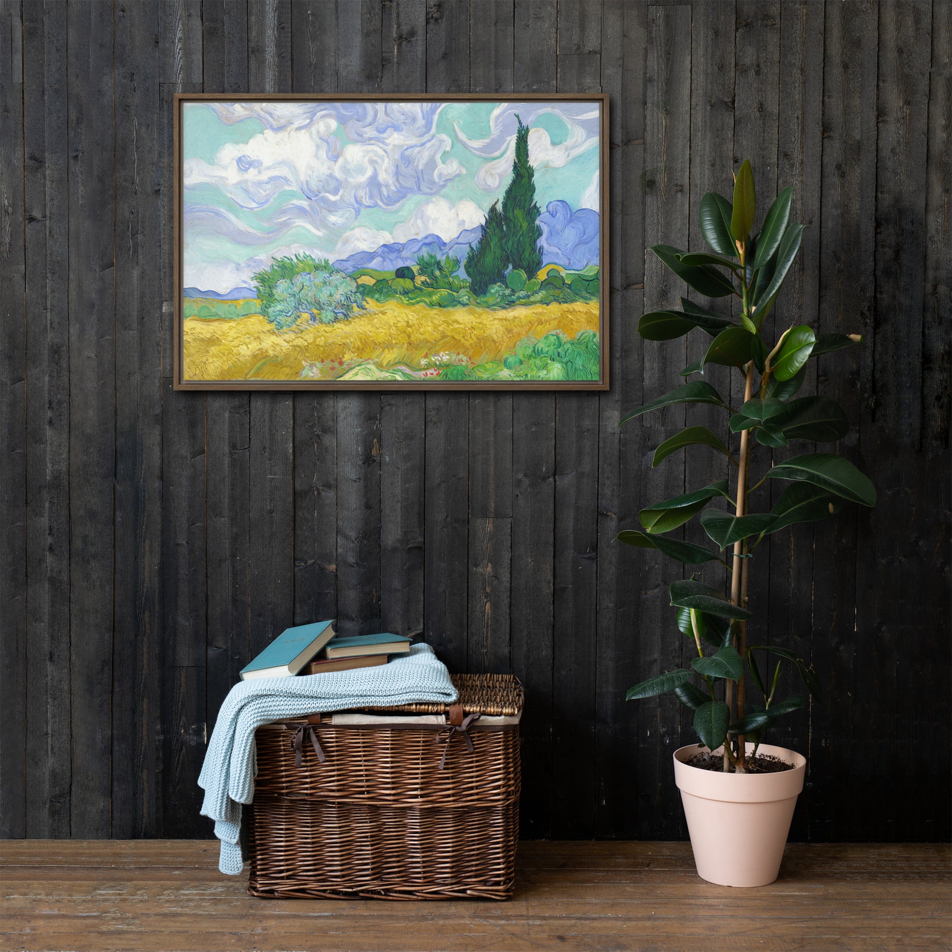 Van Gogh's 'Wheat Field with Cypresses' on a 24"x36" brown framed canvas print on a dark wooden wall with a wicker bin and plant below.
