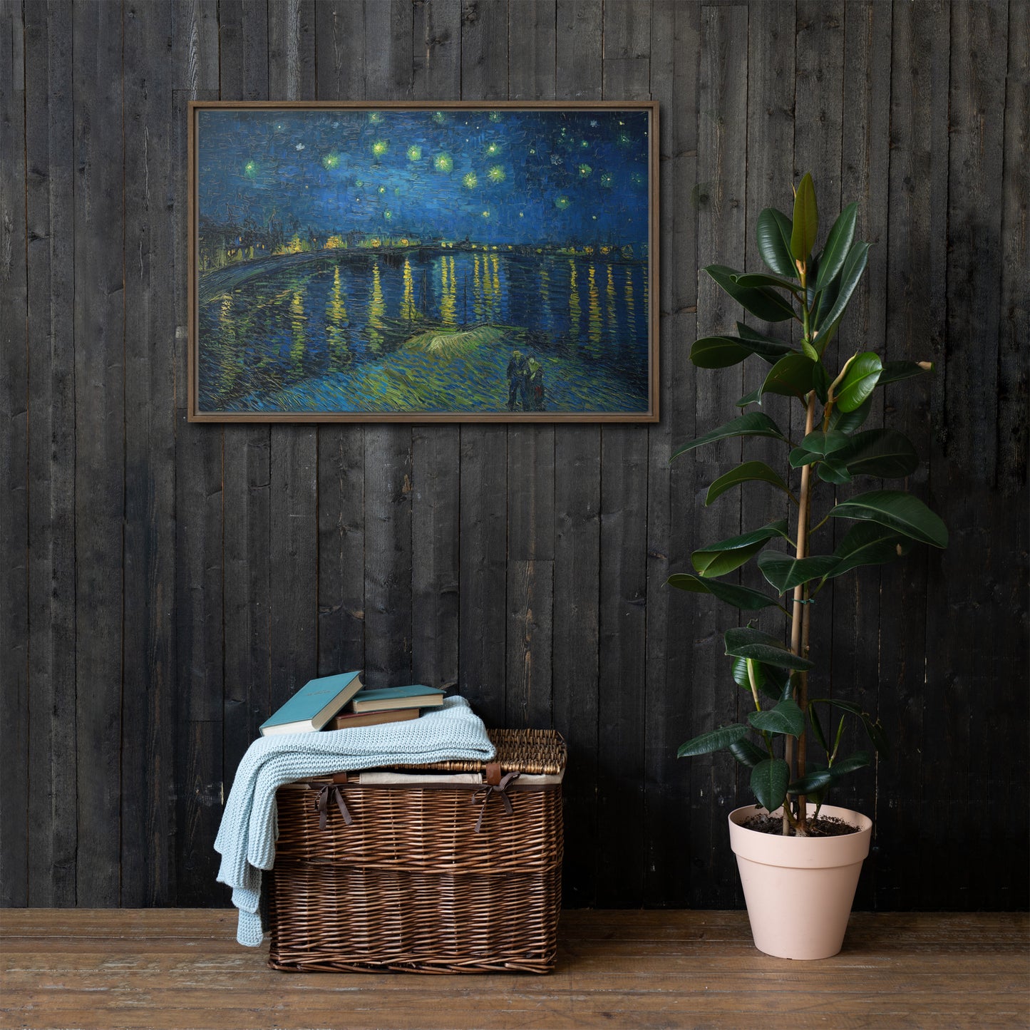Van Gogh's 'Starry Night Over the Rhone' on a 24"x36" brown framed canvas print on a dark wooden wall with a wicker bin and plant below.