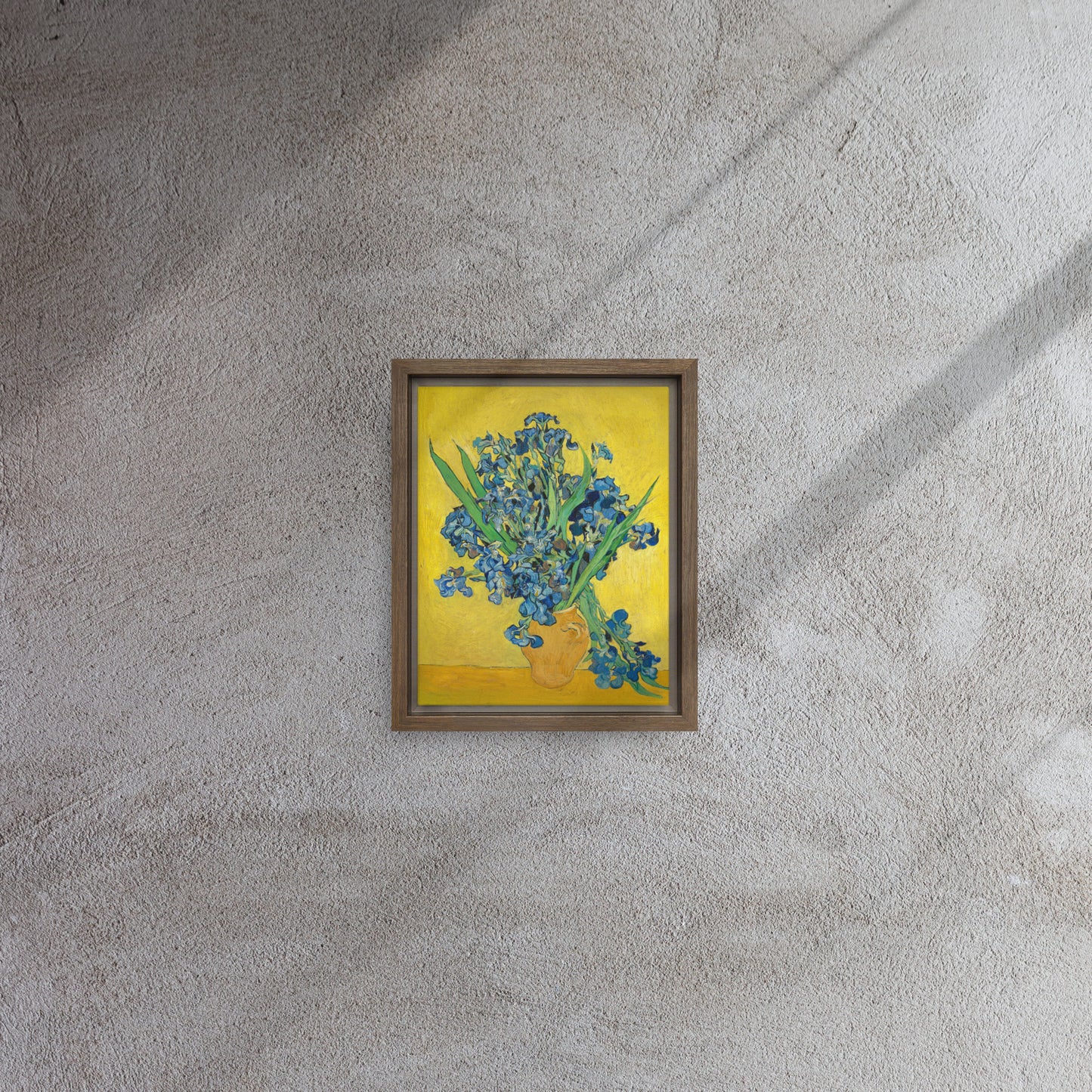 Van Gogh's 'Vase with Irises Against a Yellow Background' on a 8"x10" brown framed canvas print on a textured gray wall.